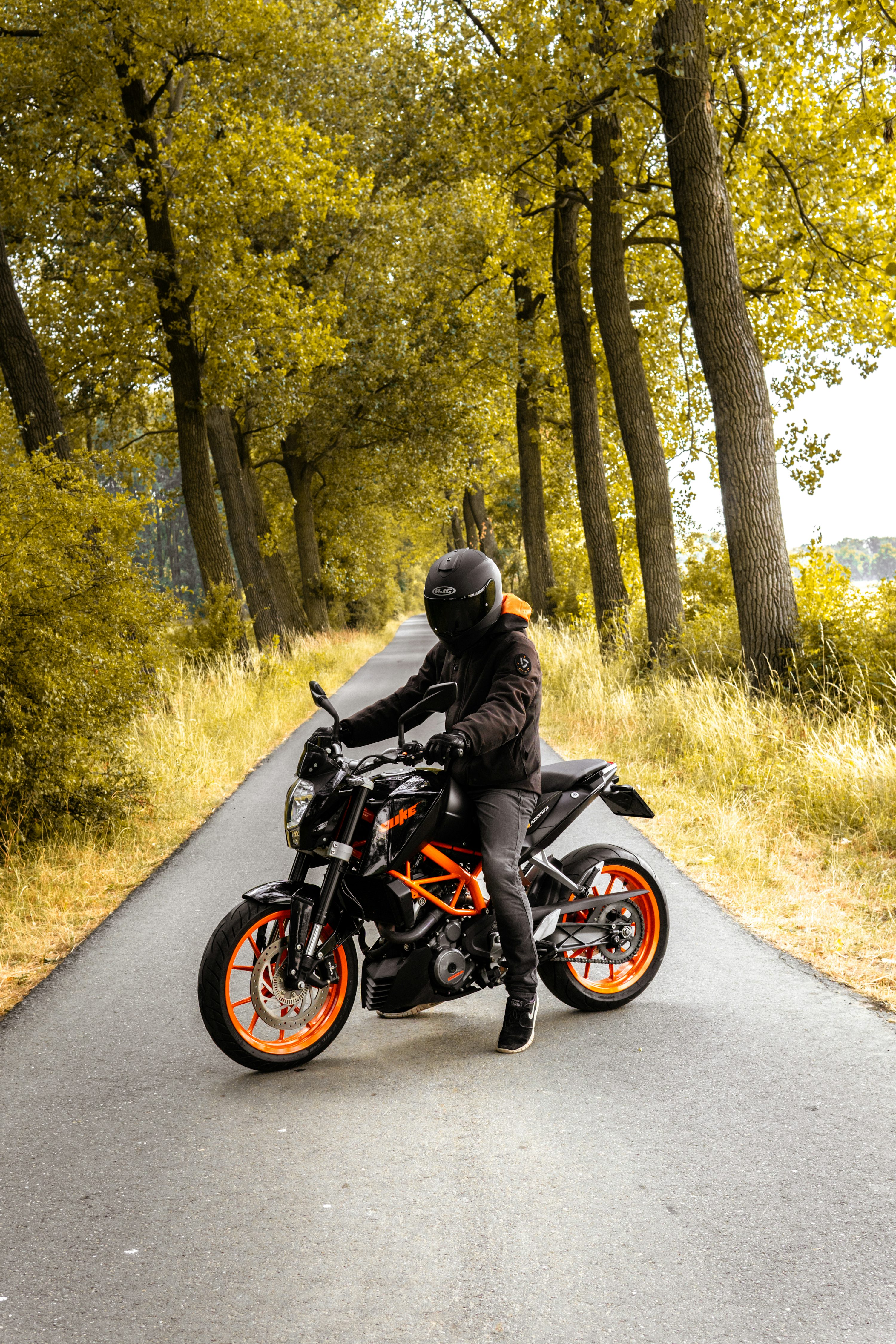 Man riding black and orange motorcycle beside trees photo