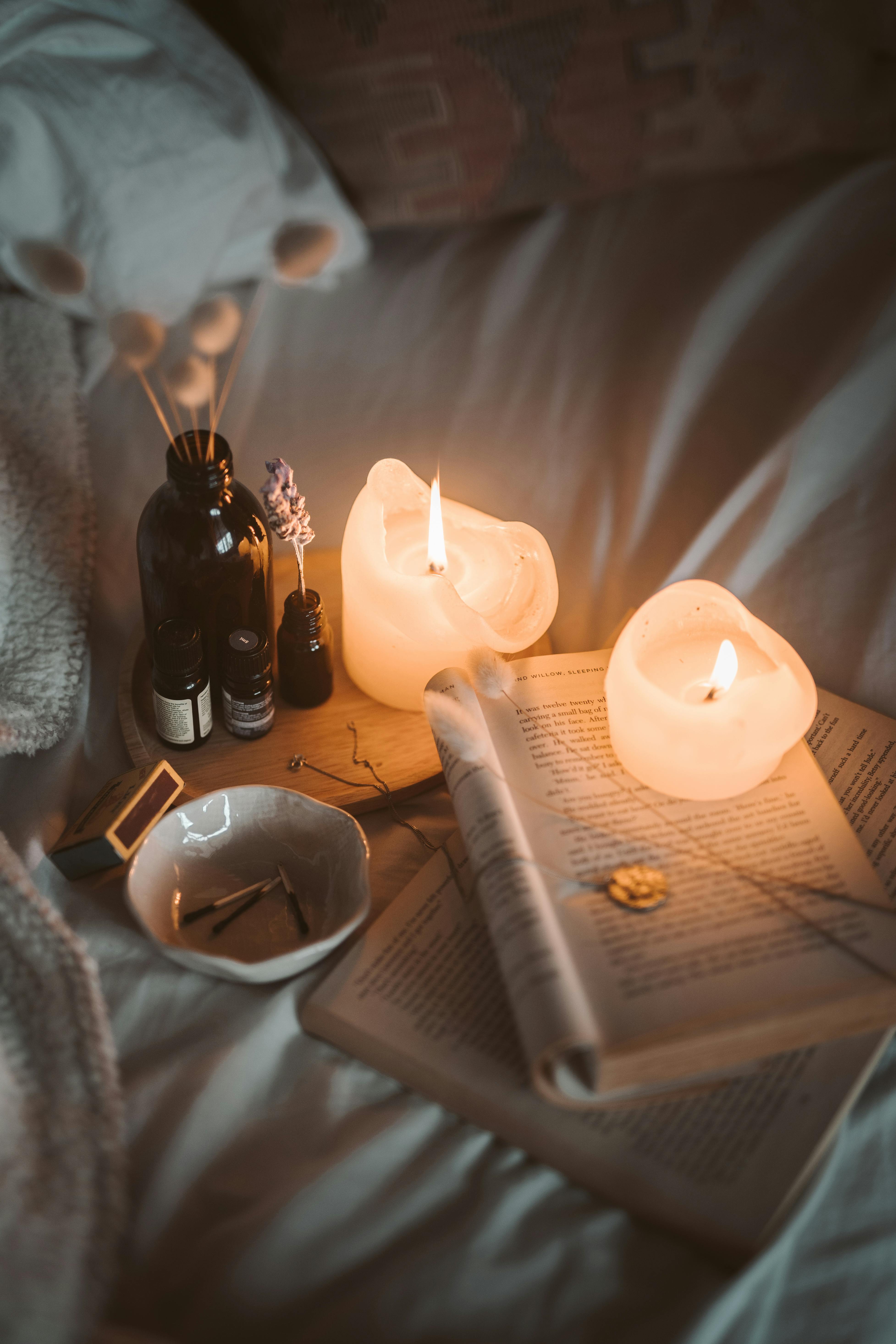 Lighted Candle on White Book Beside Black Glass Bottle · Free