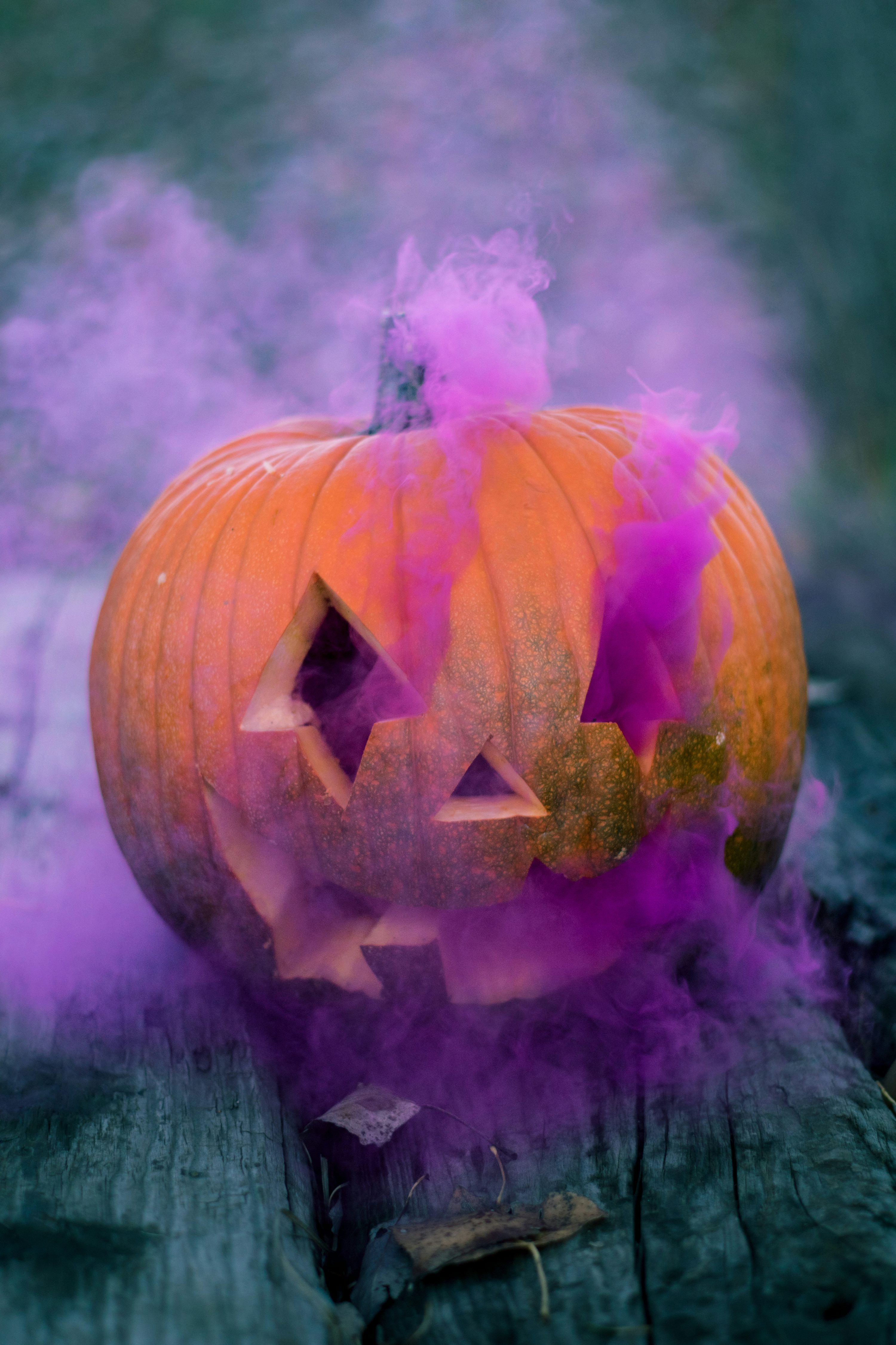 Orange Jack O' Lantern With Pink Smoke On Gray Wooden Surface Photo
