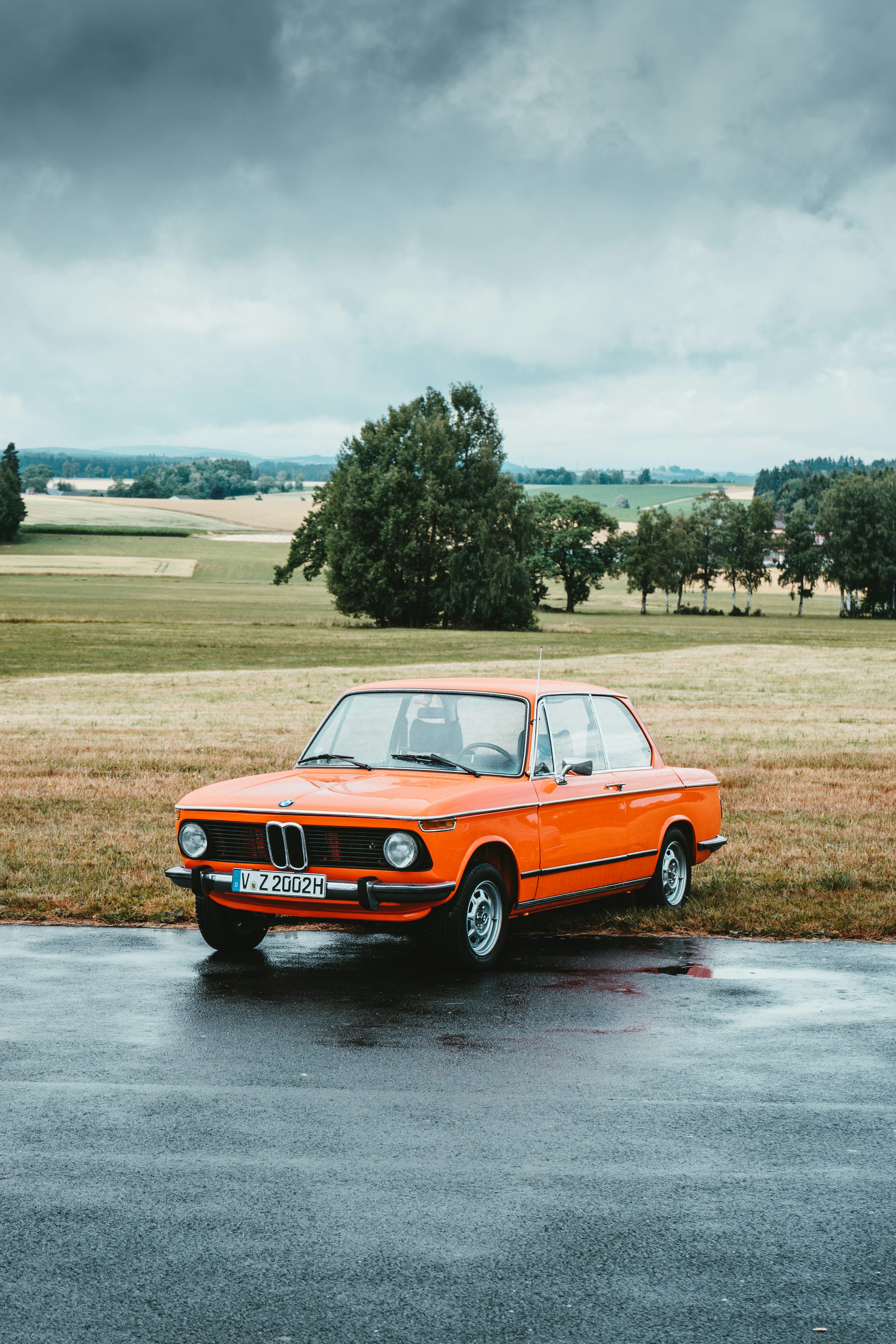 Orange classic BMW coupe parked at roadside under grey cloudy sky photo