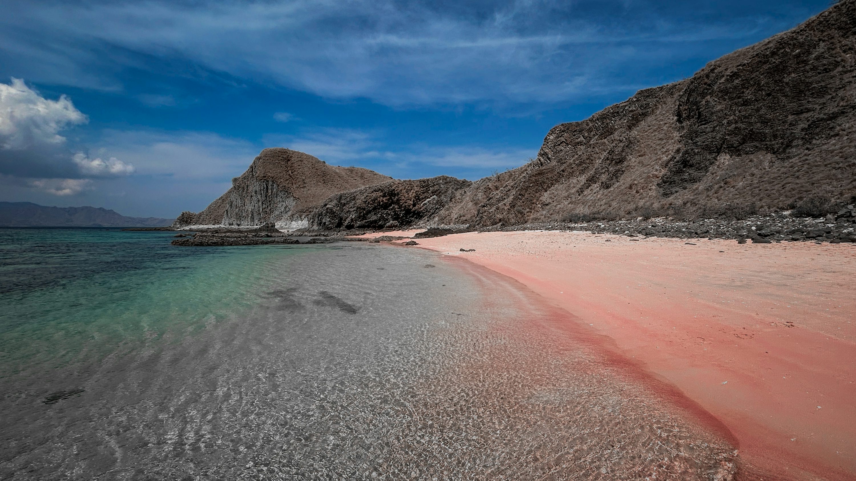 A beach with a pink sand and a mountain in the background photo