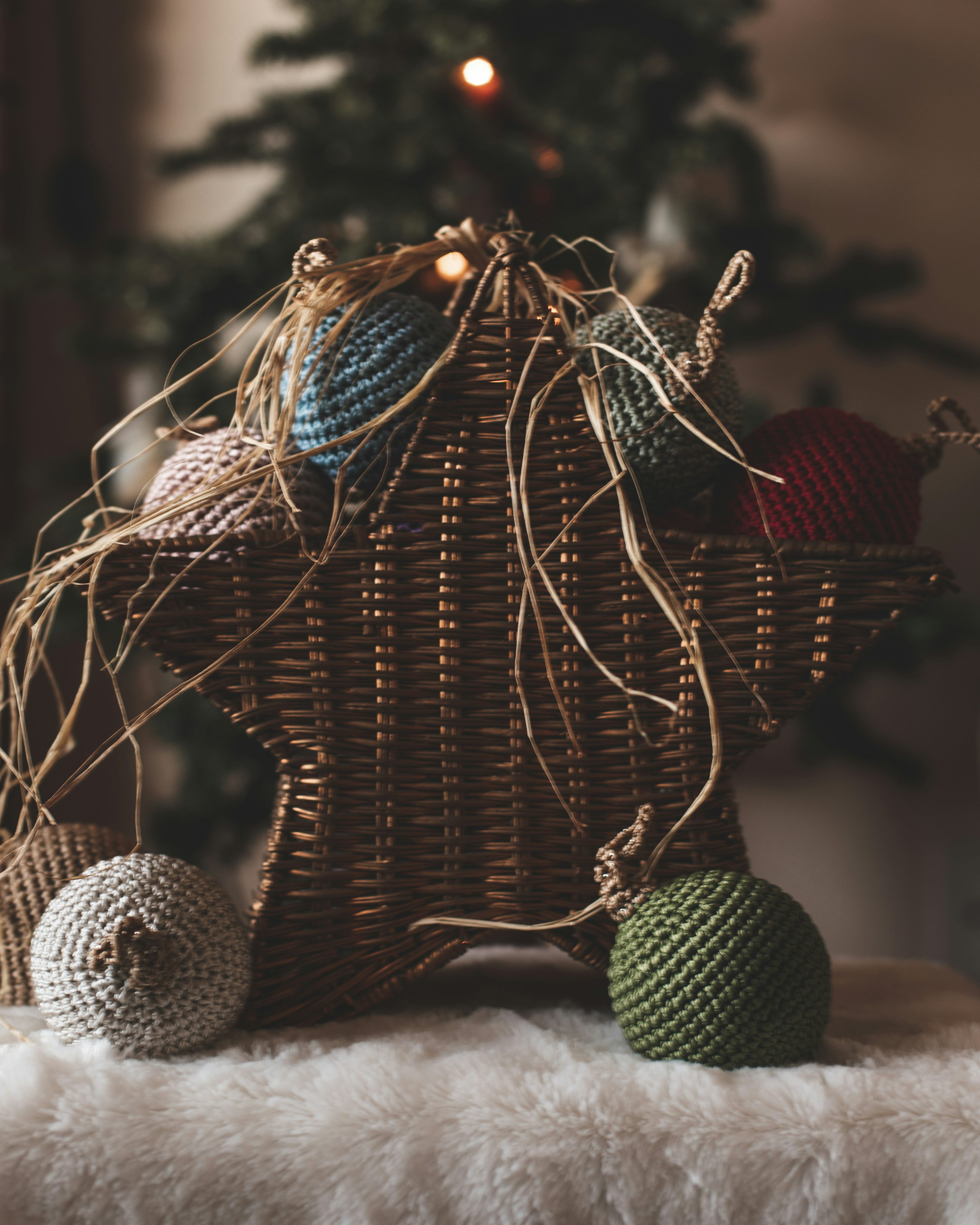 A wicker basket with balls of yarn in front of a christmas tree photo