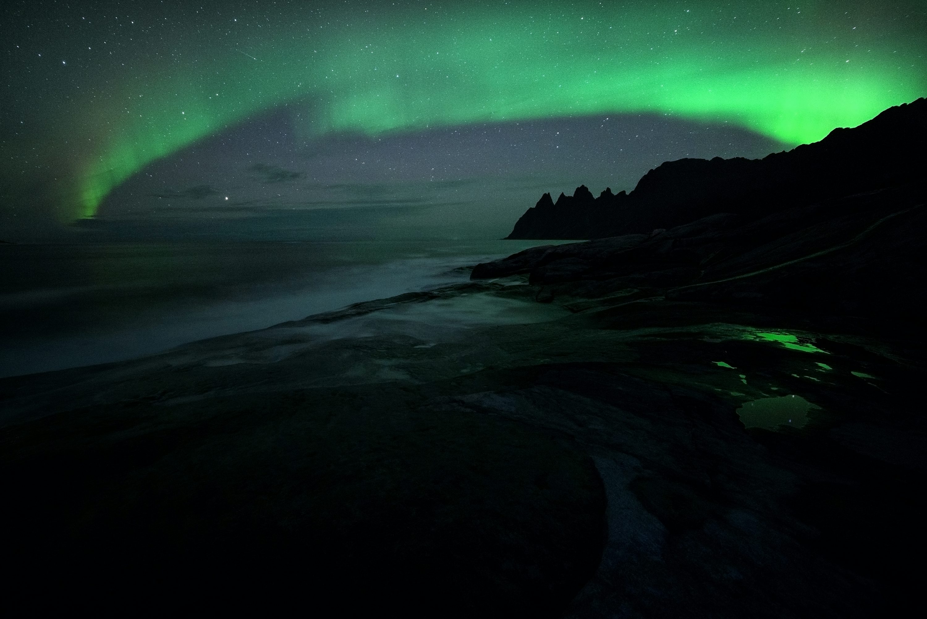 A green and black aurora over a body of water photo