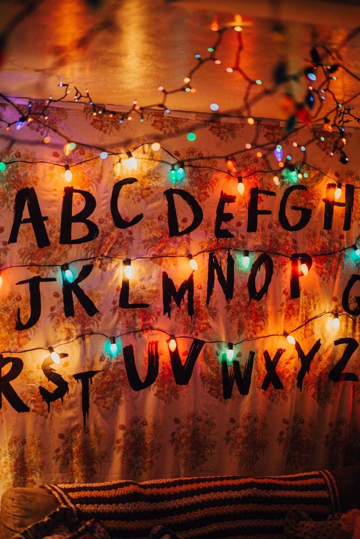 Stranger Things party decorations / Byers living room. “Wallpaper” diy using a floral sheet and iron on letters printed from the computer onto dark fabric transfer paper. Christmas lights plugged into a