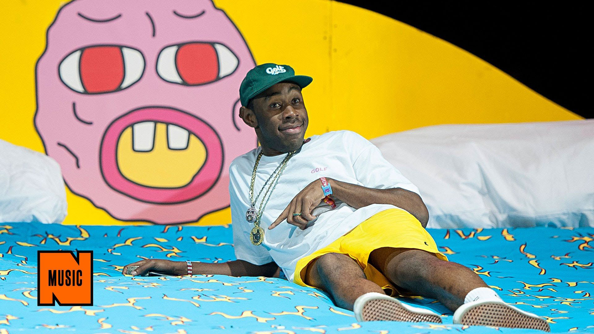 Tyler The Creator Is Lying On Blue Bed Wearing White Tshirt And Yellow Shorts Posing For A Photo HD Music Wallpaper