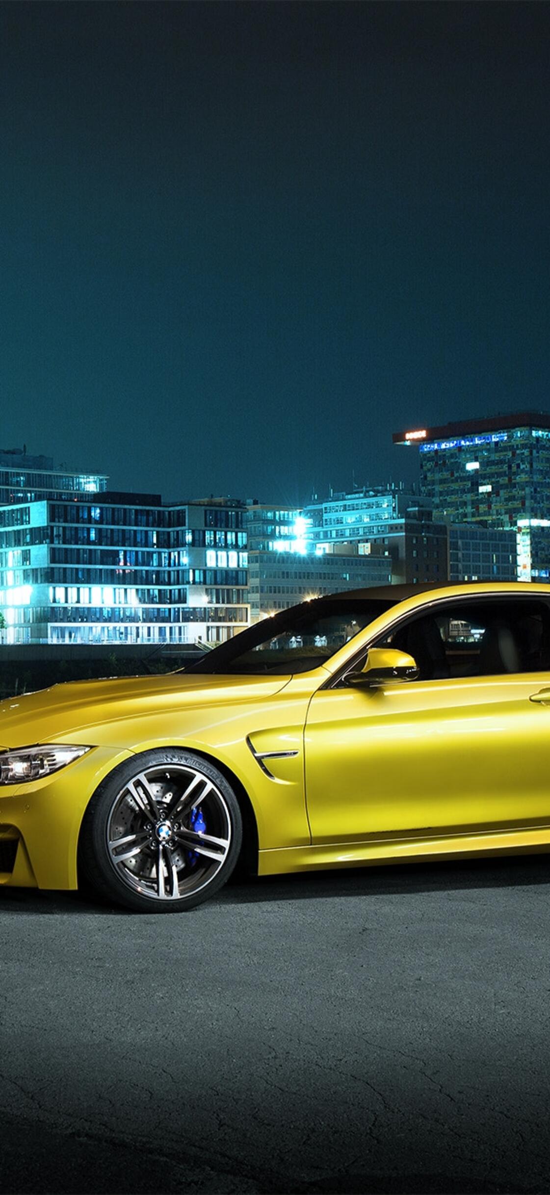 A gold BMW F82 M4 stands against the backdrop of a city at night · 1125x2436 iPhone XS free photo from 20002000 and wallpaper