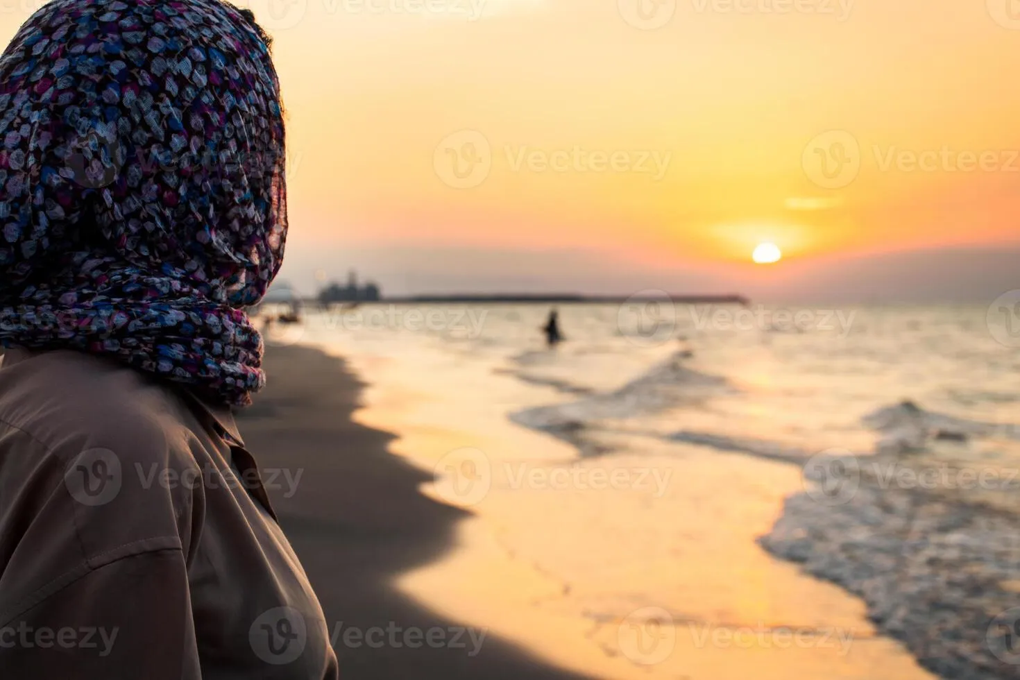 Beautiful muslim woman in hijab standing by the river at sunset