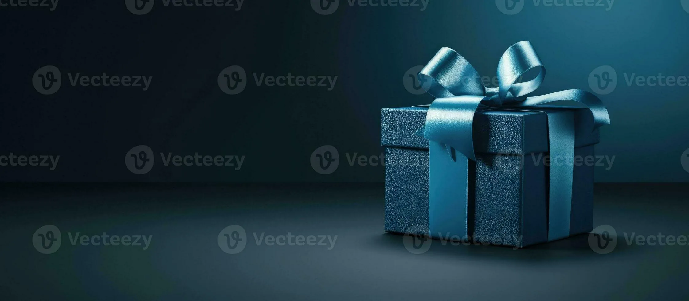 side view monochrome image of a small luxury gift box with a blue bow on a dark blue background