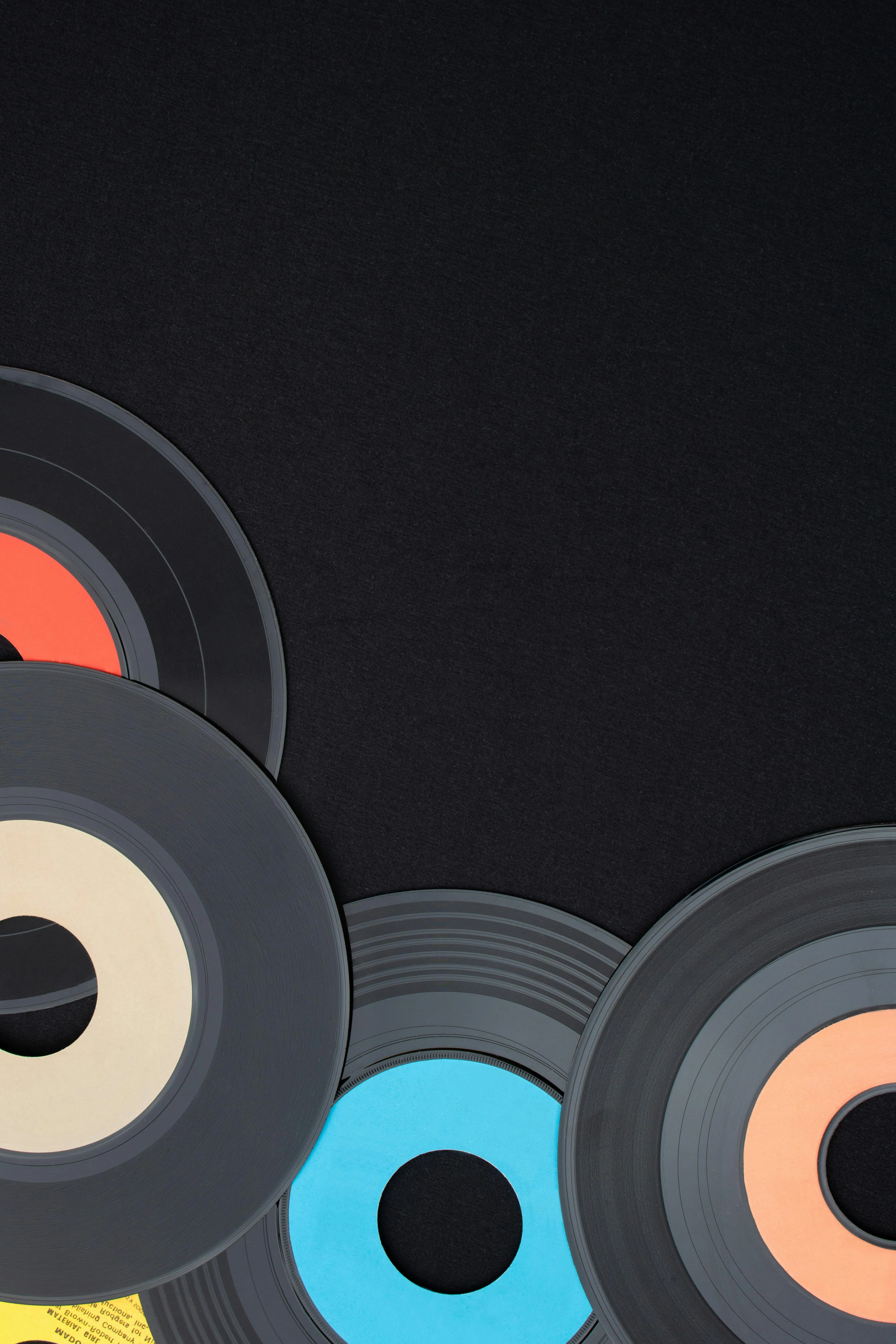Multi colored 7 inch single vinyl records on a black background placed on bottom left corner with empty space for text. Top down view flat lay. Retro or music concept · Free