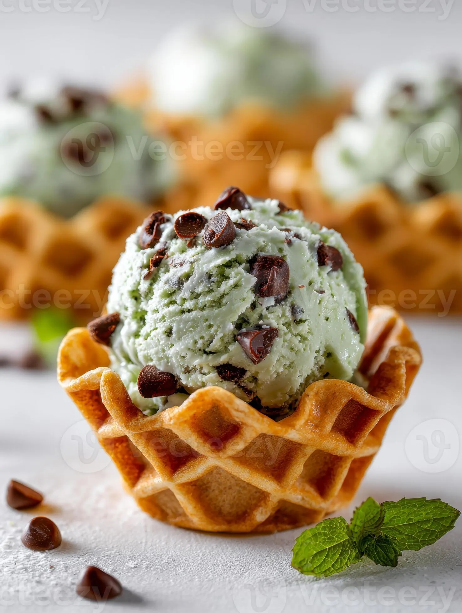 Mint chocolate chip ice cream served in a golden waffle bowl with fresh mint leaves and scattered chocolate pieces on a light surface, styled for dessert photography