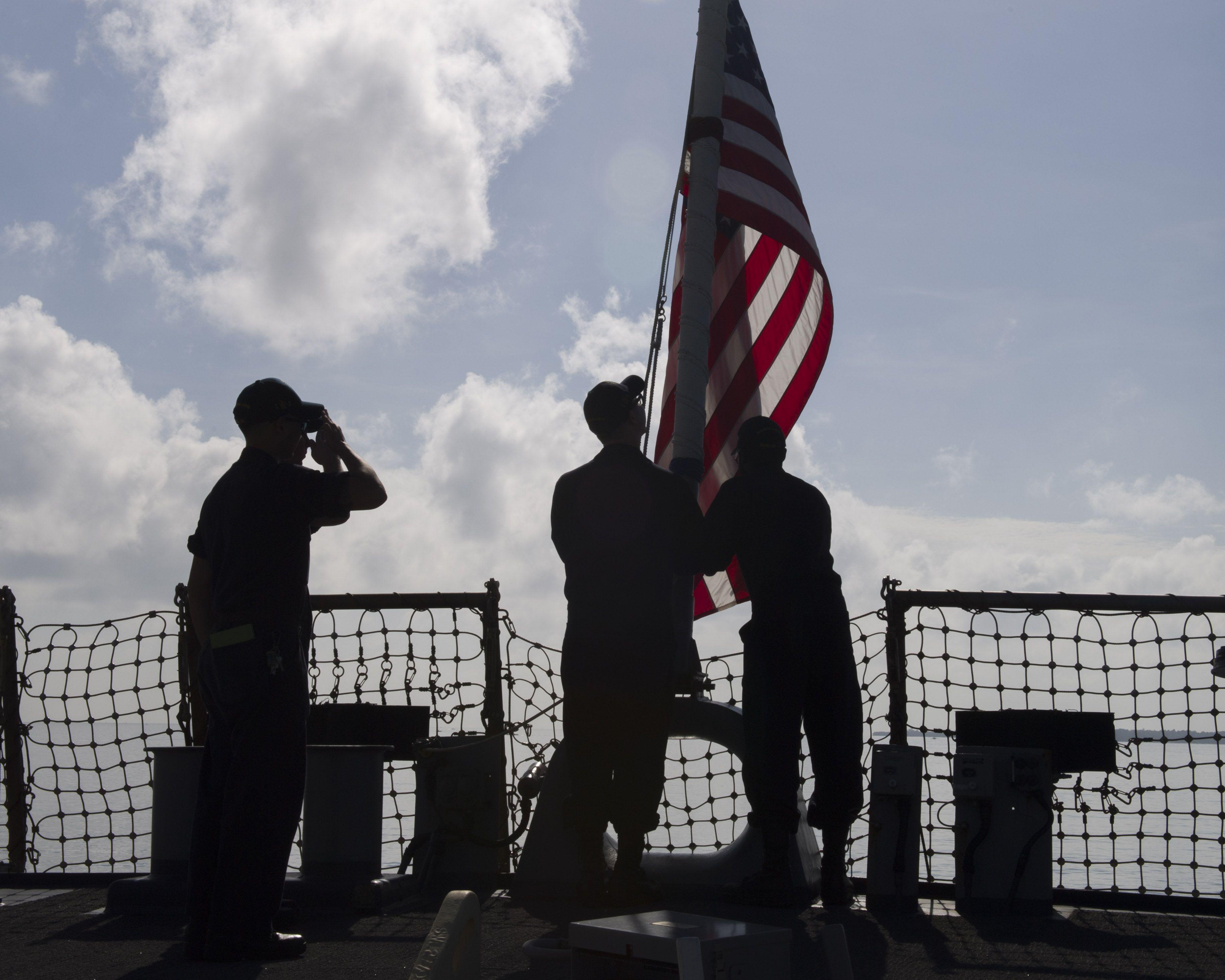 Sailors lower the ensign on the flight deck of USS John S