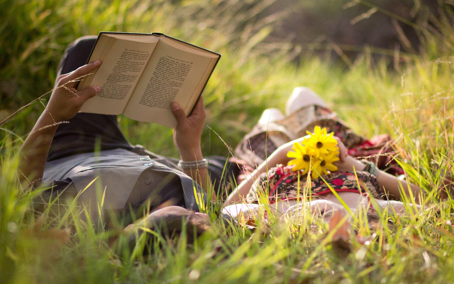 Romantic couple lying on the grass, reading the book