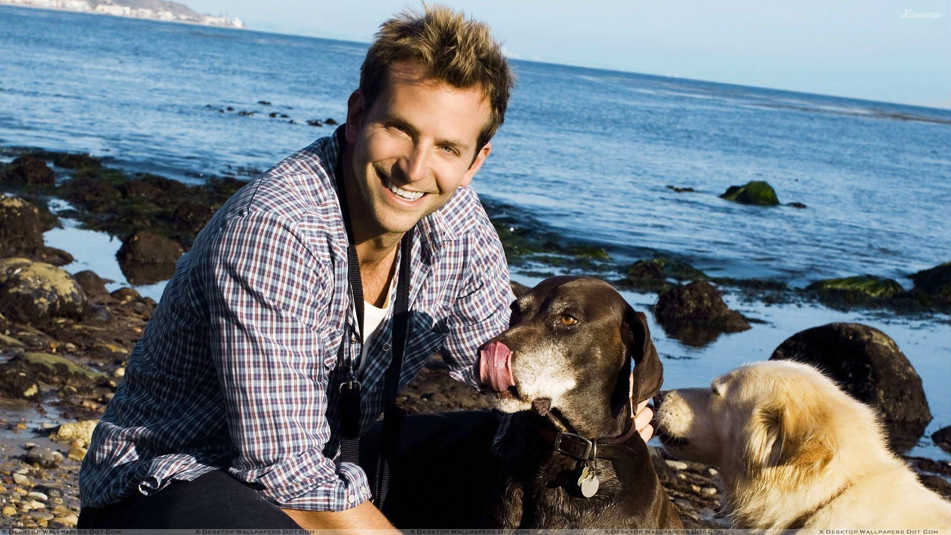 Bradley Cooper Smiling Sitting At Sea Side With Dogs Wallpaper