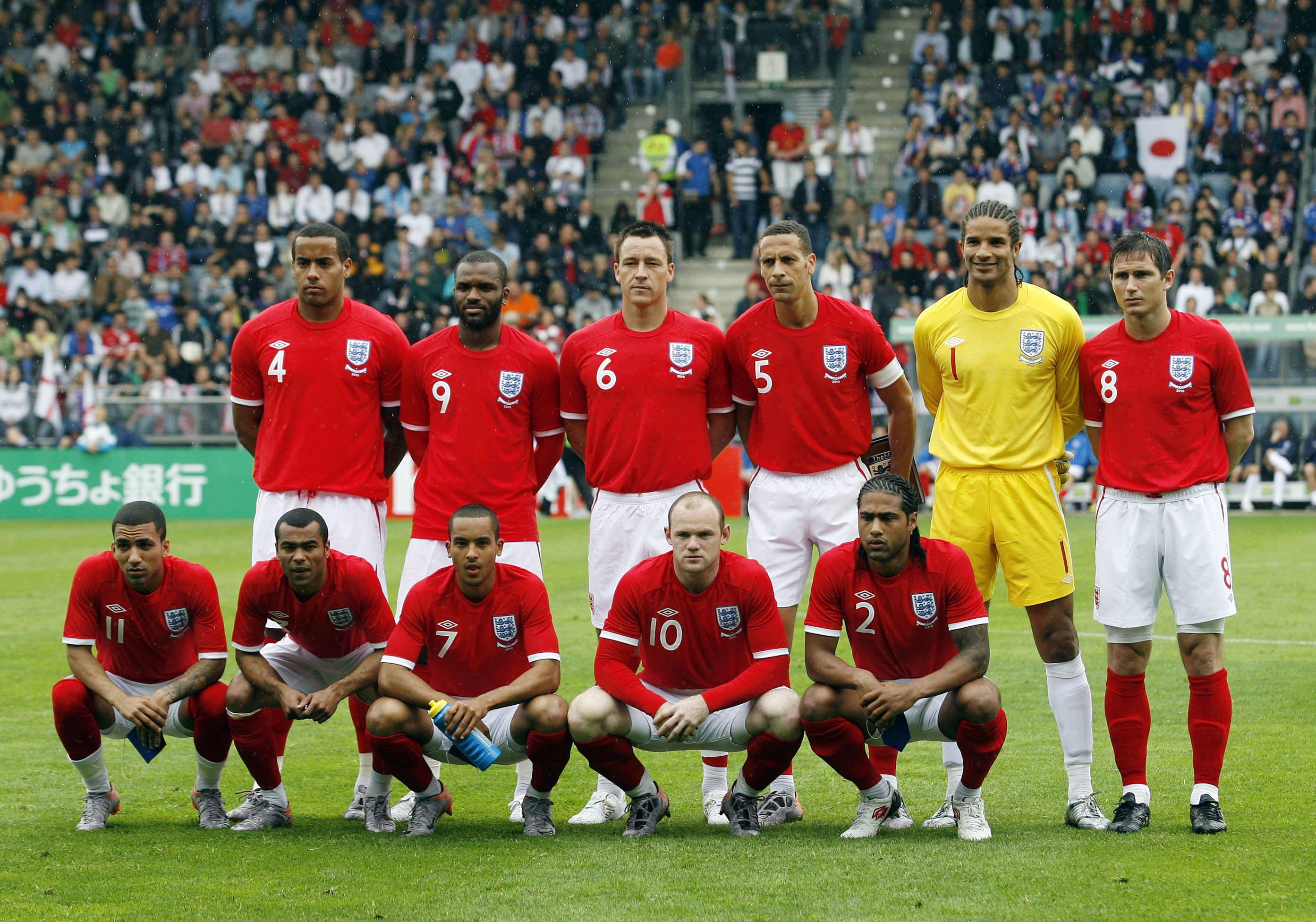  The English National Football Team is lined up in their red jerseys, white shorts, and red socks, with the Serbian team in their white jerseys, blue shorts, and white socks lined up across from them.