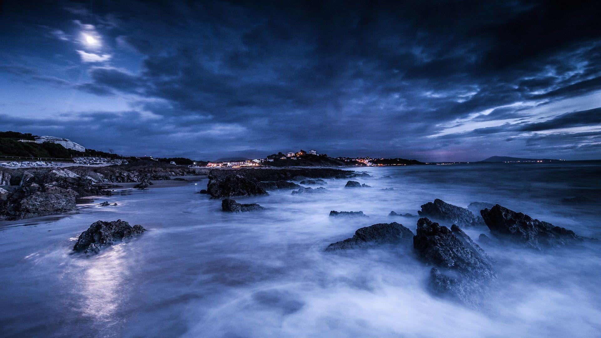 Sea, night, moon, clouds, rocks, shore, lights, blue wallpaper