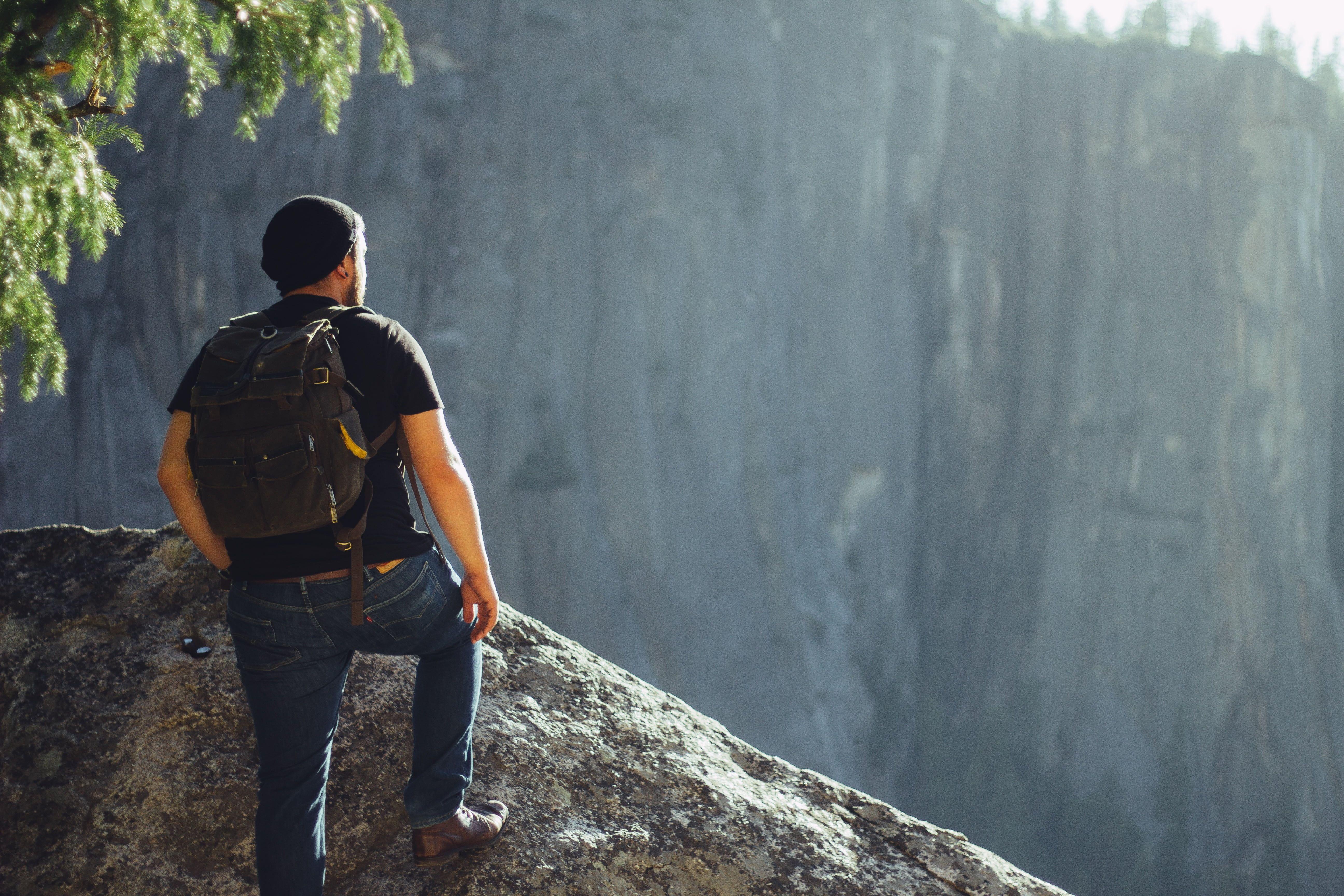 Man on top of rock formation wearing black backpack and shirt HD