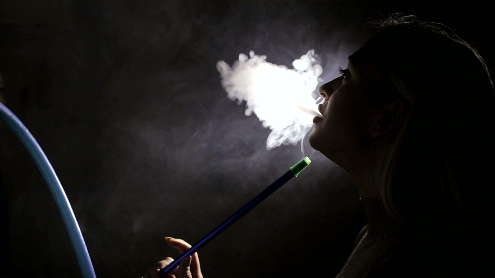 Silhouette of a girl who smokes hookah on a black background