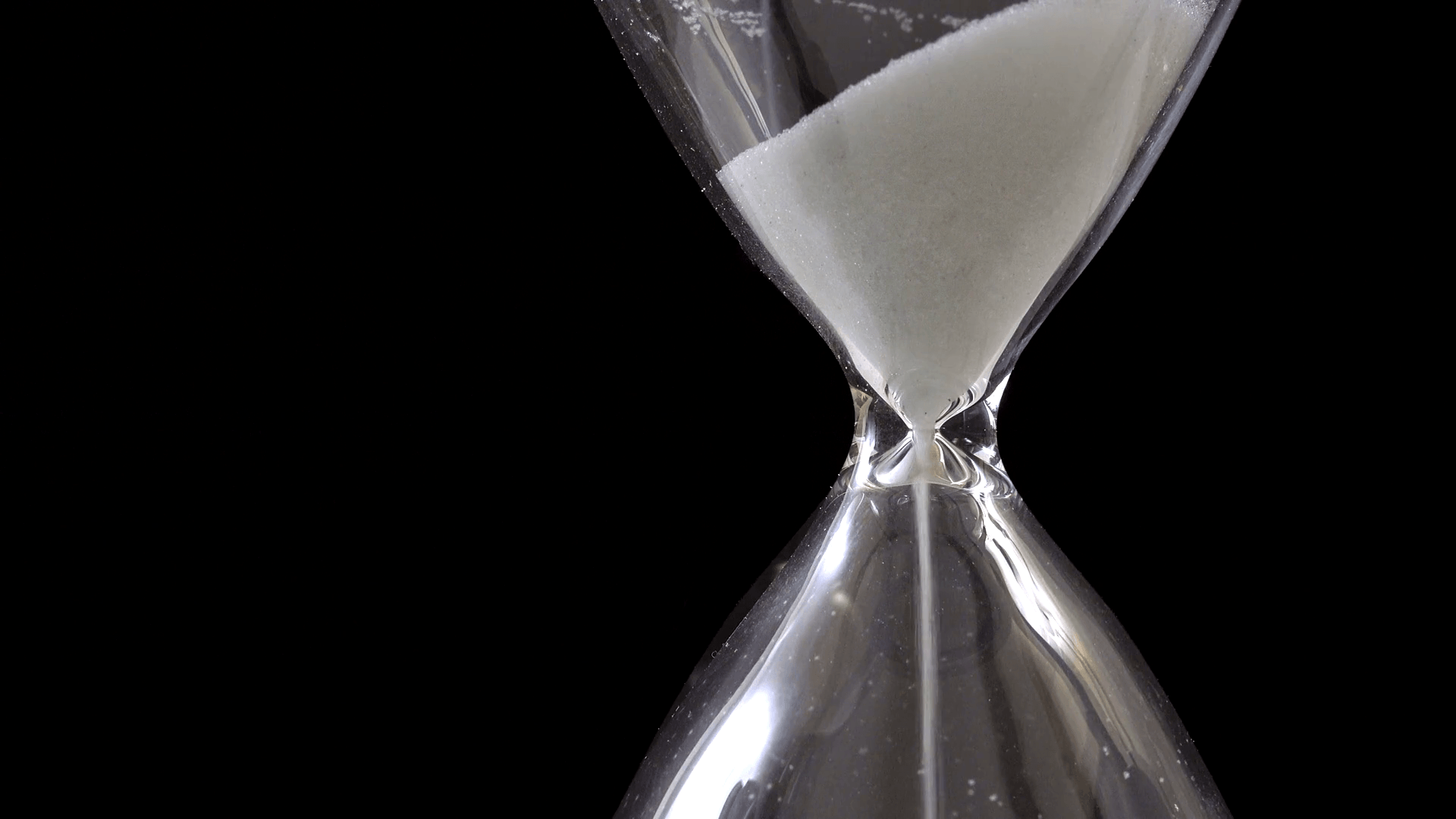 Sand pouring in hourglass on black background, time passing concept