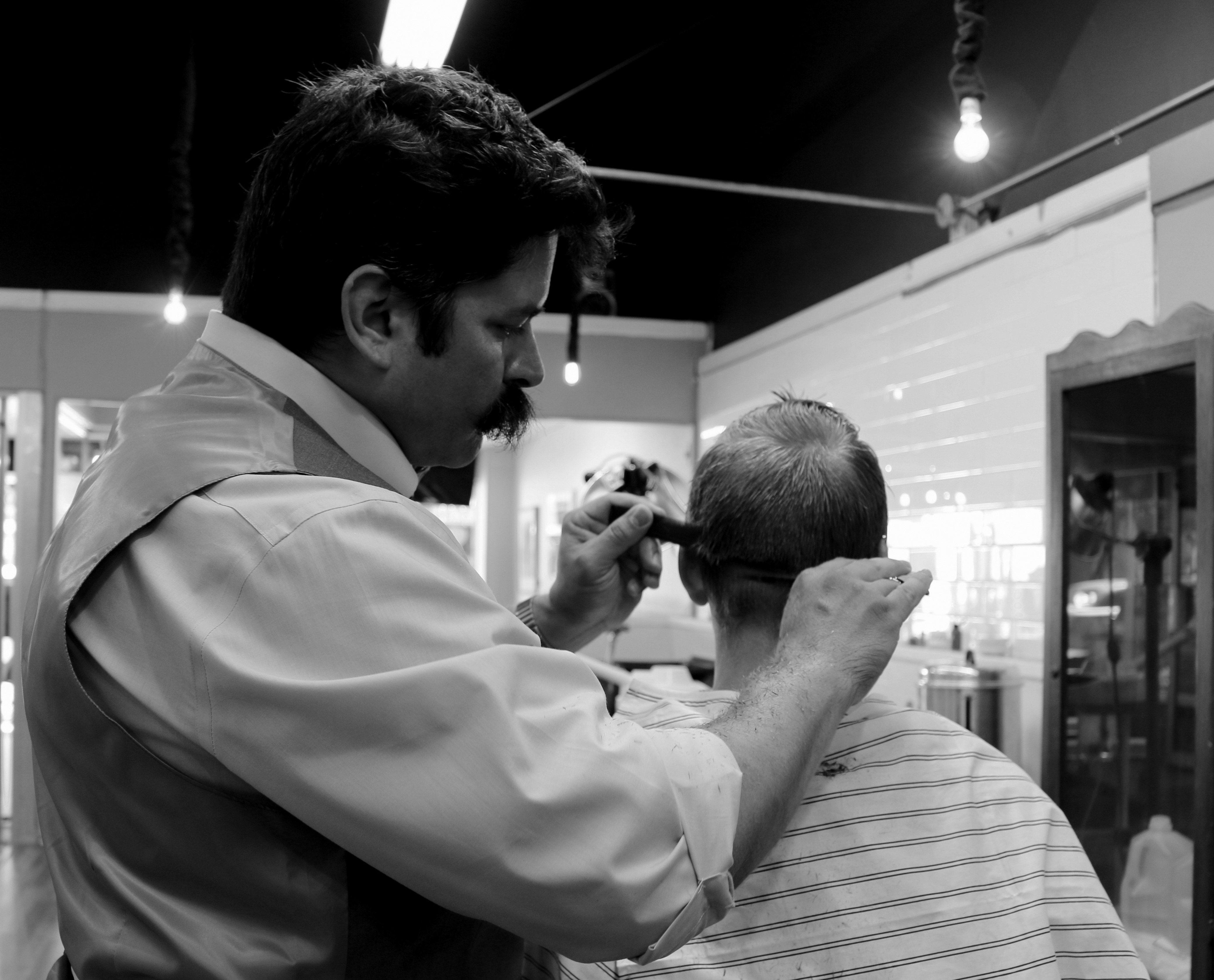 man cutting hair of boy in grayscale photography free image