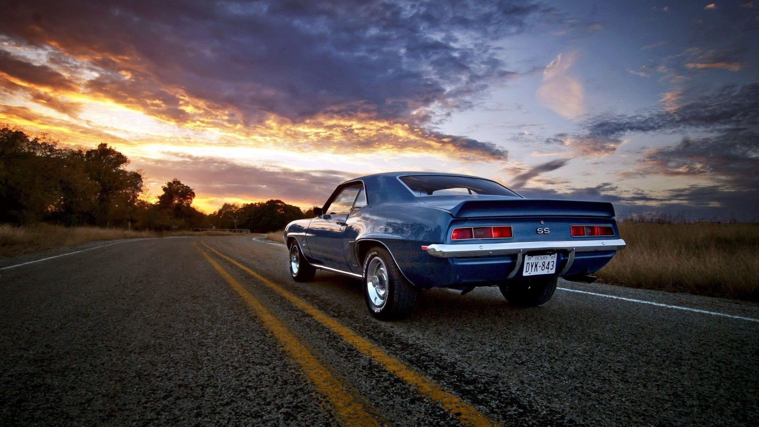 Classic blue Ford Mustang on open road during golden hour HD