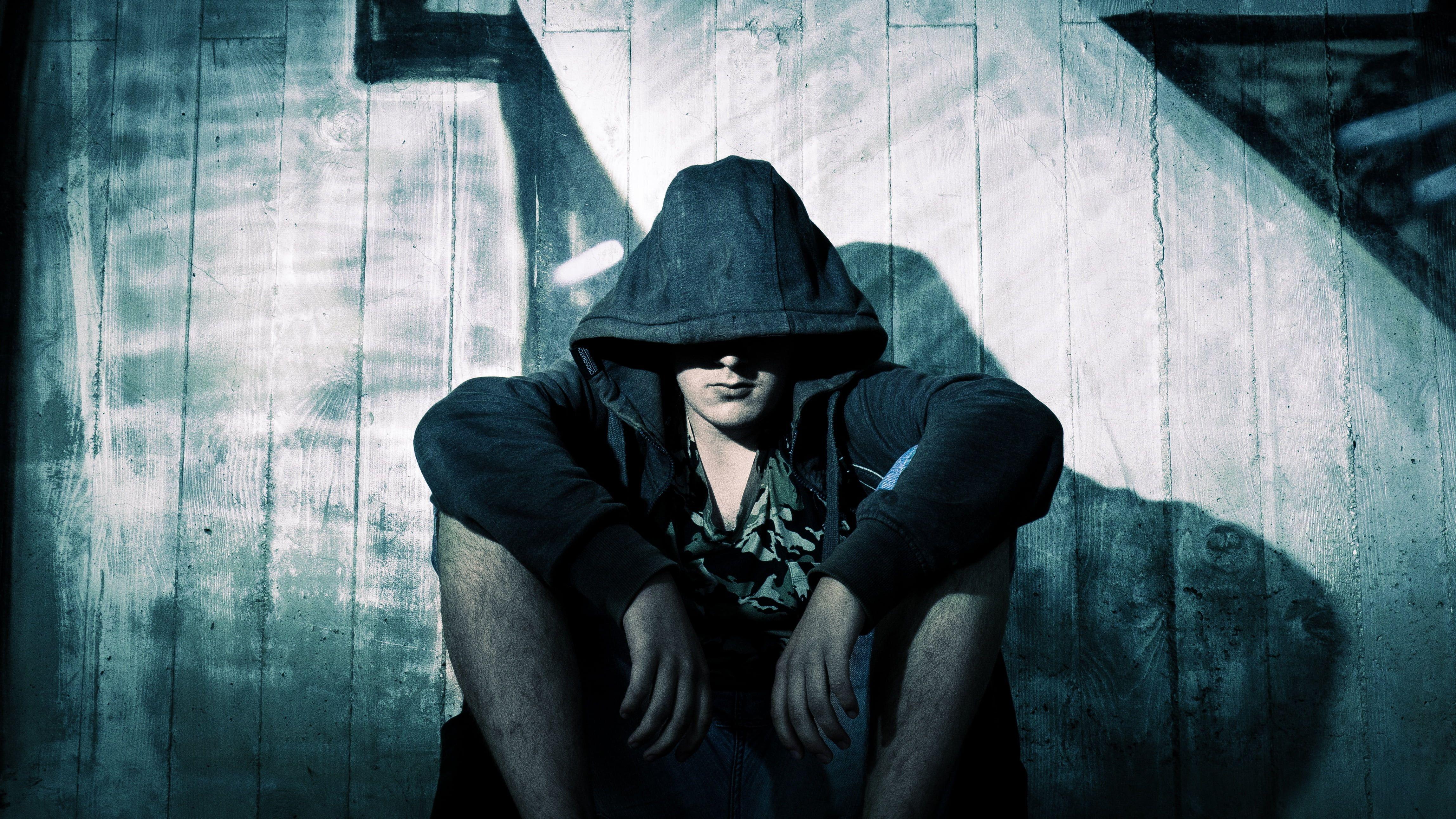 Man in black hoodie sitting beside wooden wall HD wallpaper