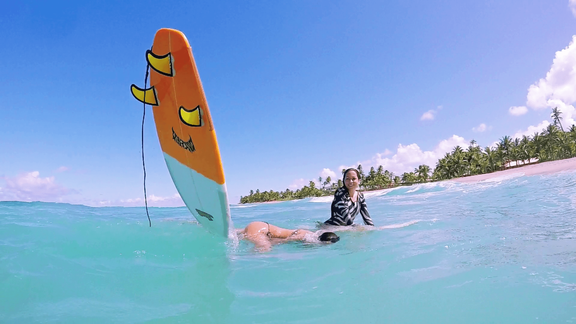 Two Surf Girls Sitting On Surfboards Loosing Balance And Falling Off