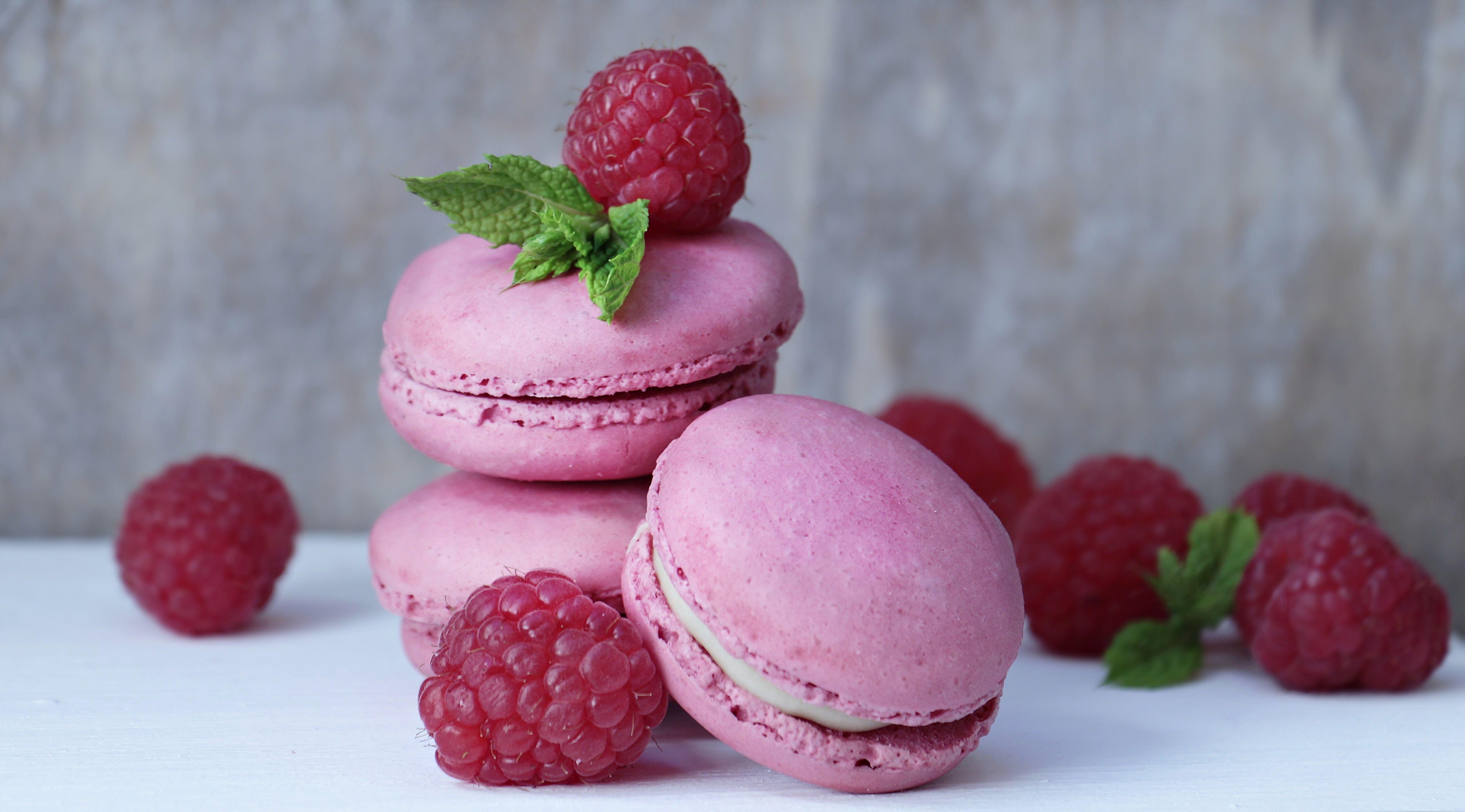 Three pink French macaroons surrounded by raspberries HD wallpaper