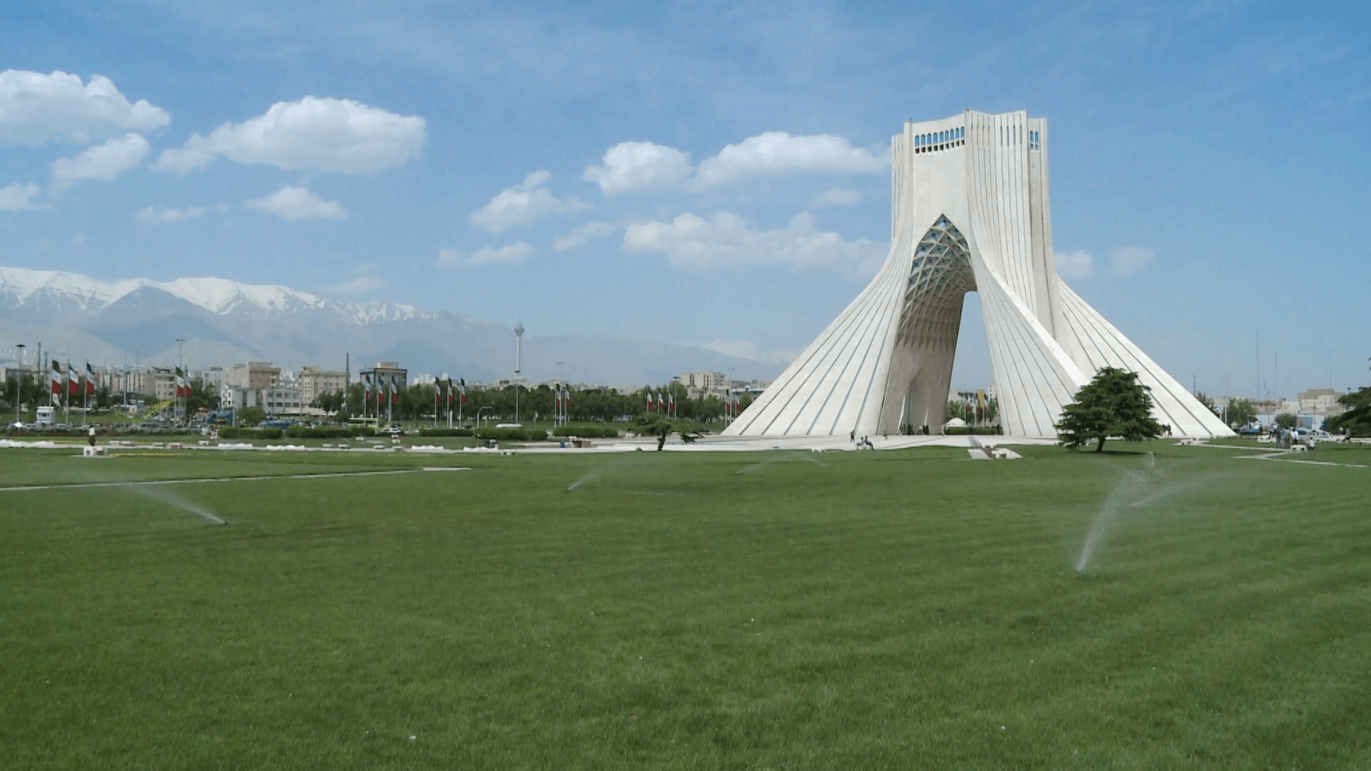 Pan left from Iranian flags to Azadi Tower, Milad Tower in back