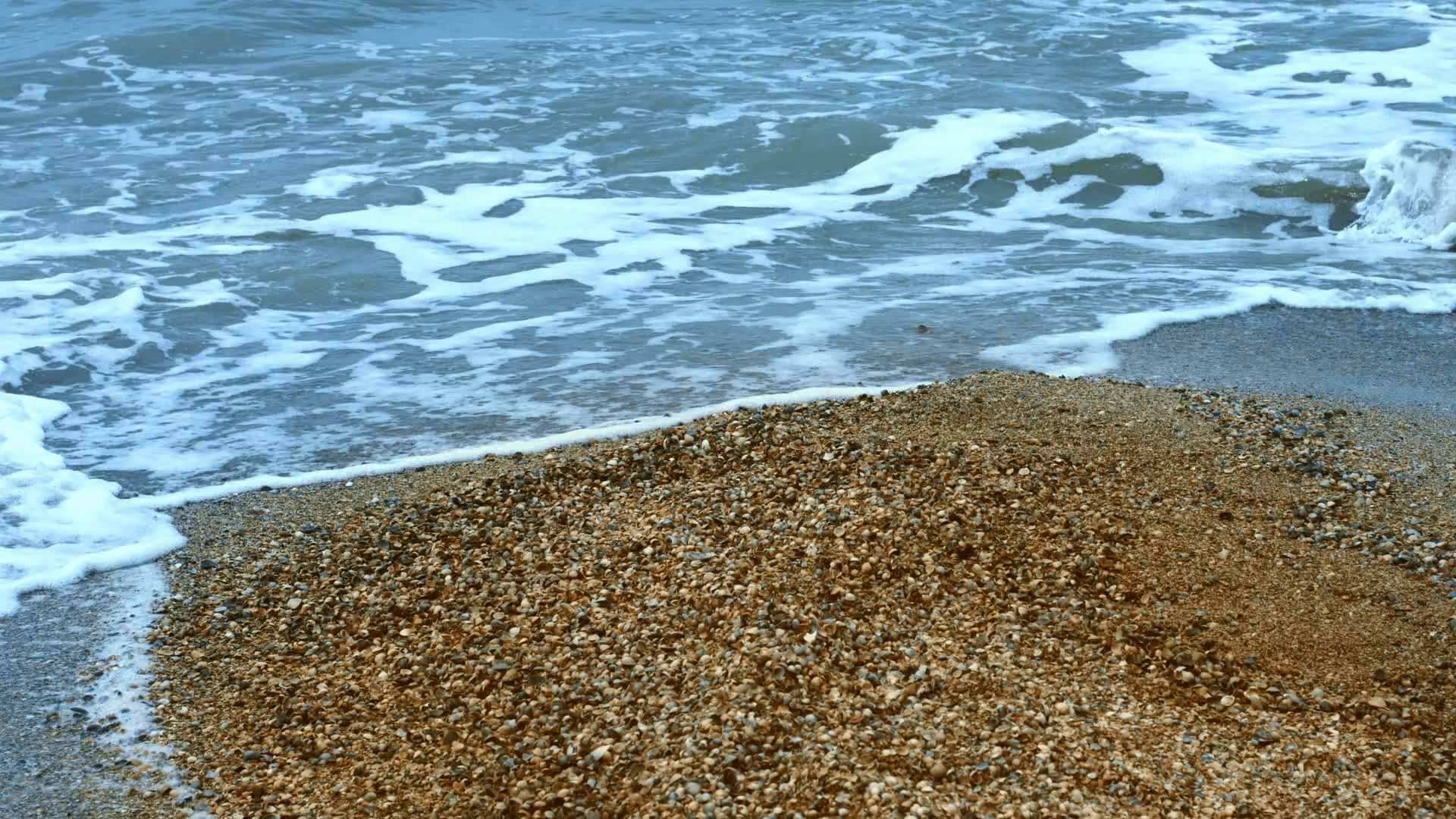Sea foam on sandy shore at summer beach. Stormy sea waves with foam