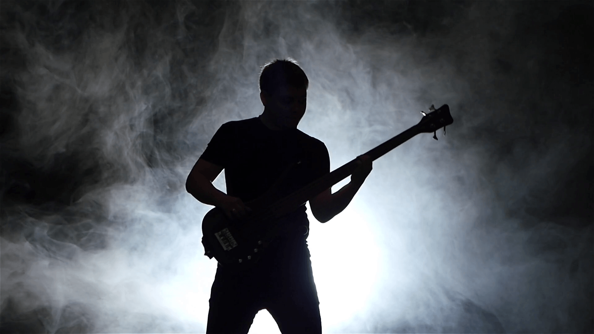 Dark background with smoke. Playing man on black bass guitar Stock