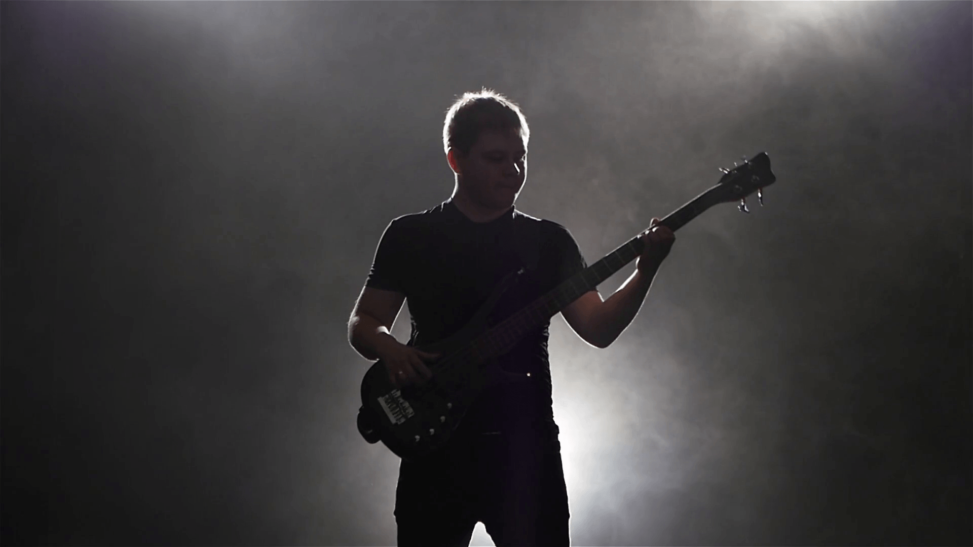 Playing man on black bass guitar. Dark background with backlight