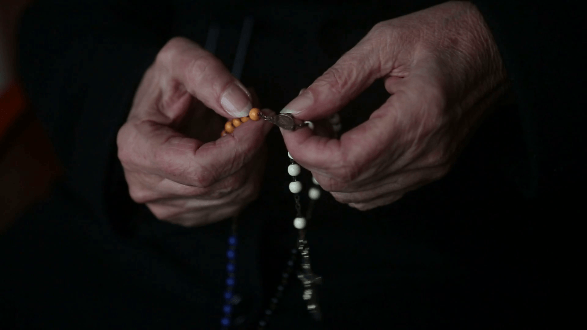 closeup of old woman's hands praying and holding a rosary Stock