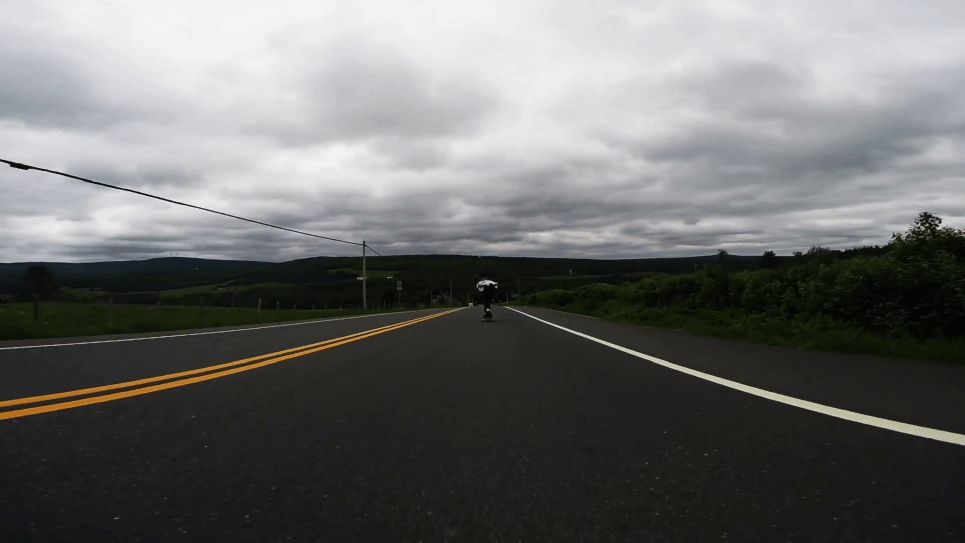 Professional skateboarder skating fast downhill the empty countryside road on longboard on cloudy day, low angle 4k shot Stock Video Footage
