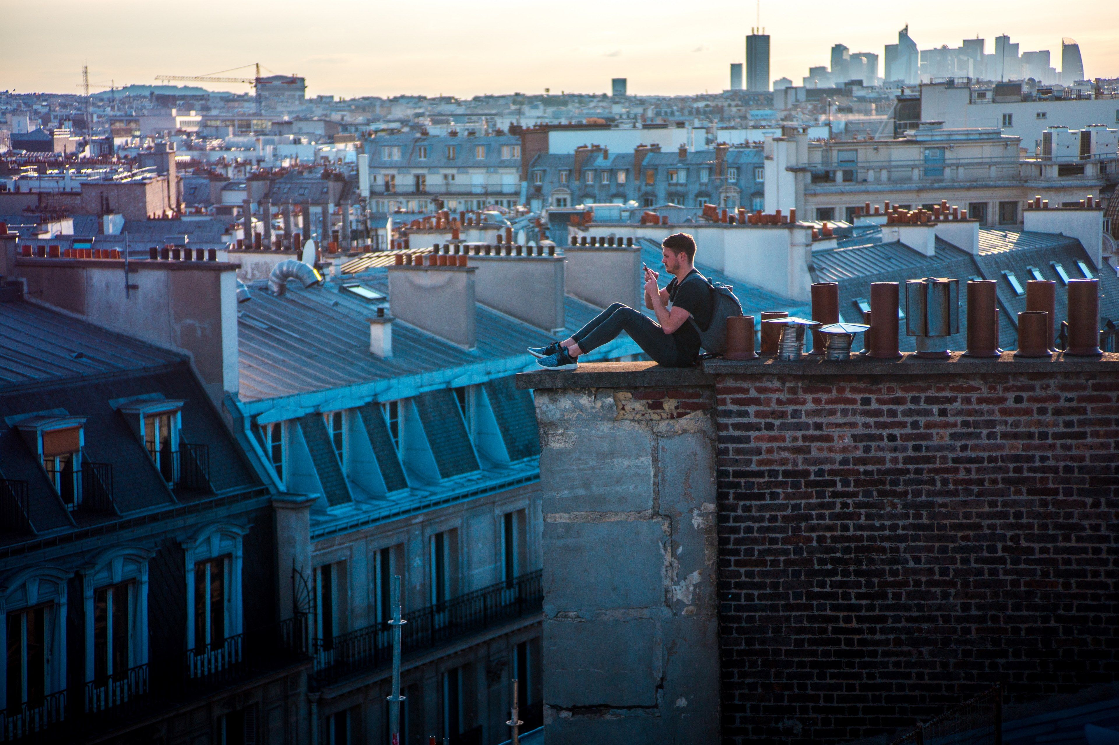 a young man sitting on the edge of a roof next to a chimney paris
