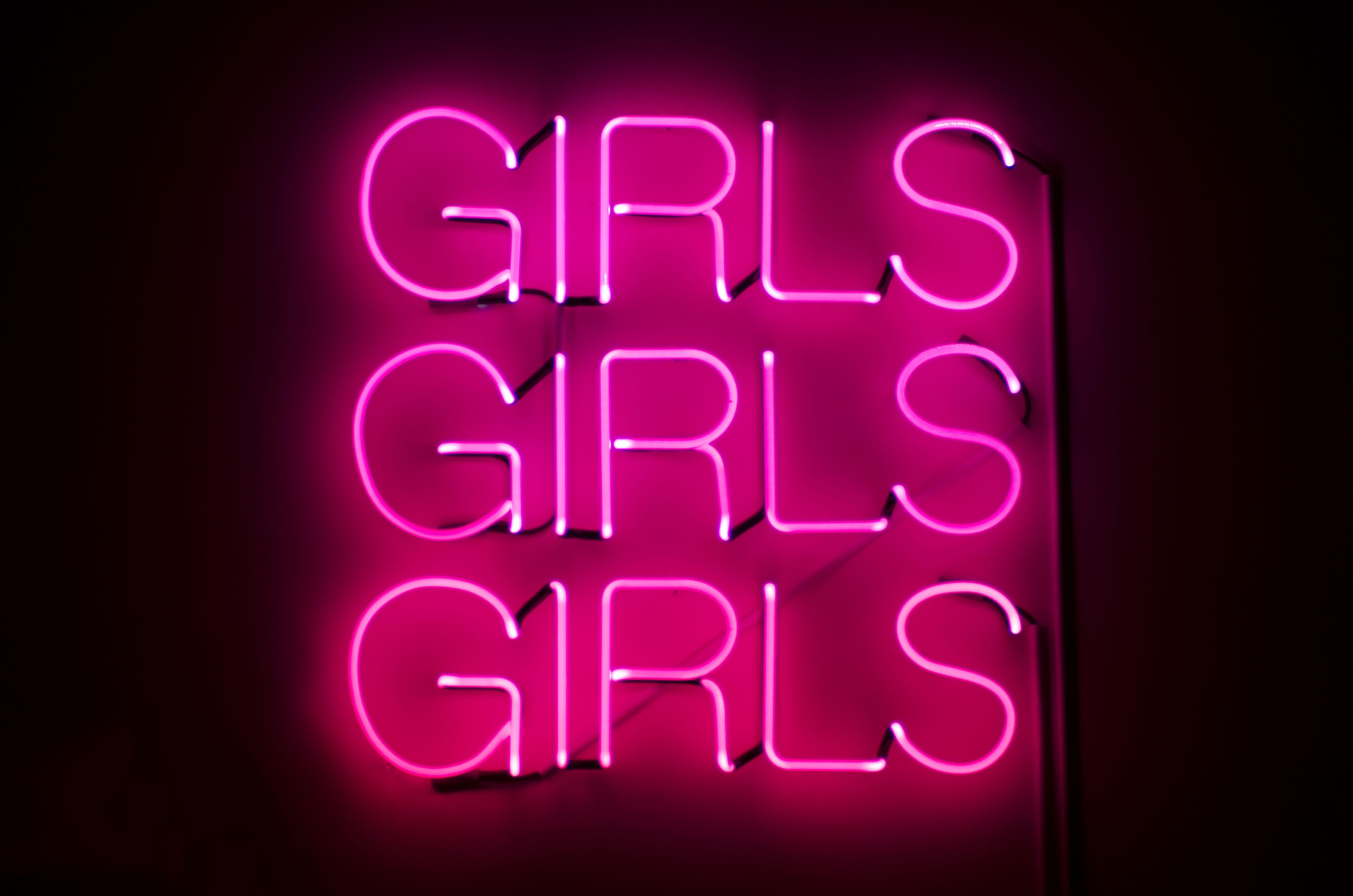 Girls Girls Girls sign glows in racy pink neon against dark night