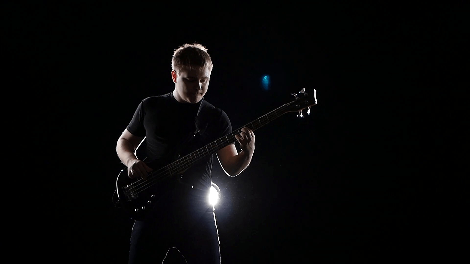 Dark background with smoke. Playing man on black bass guitar Stock