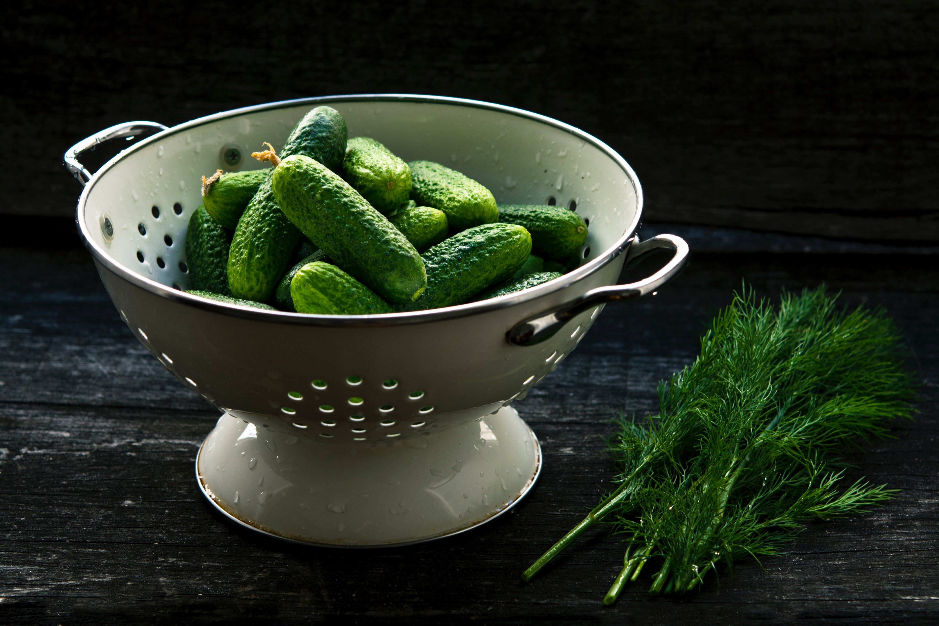 colander with fresh cucumbers on a table next to dill