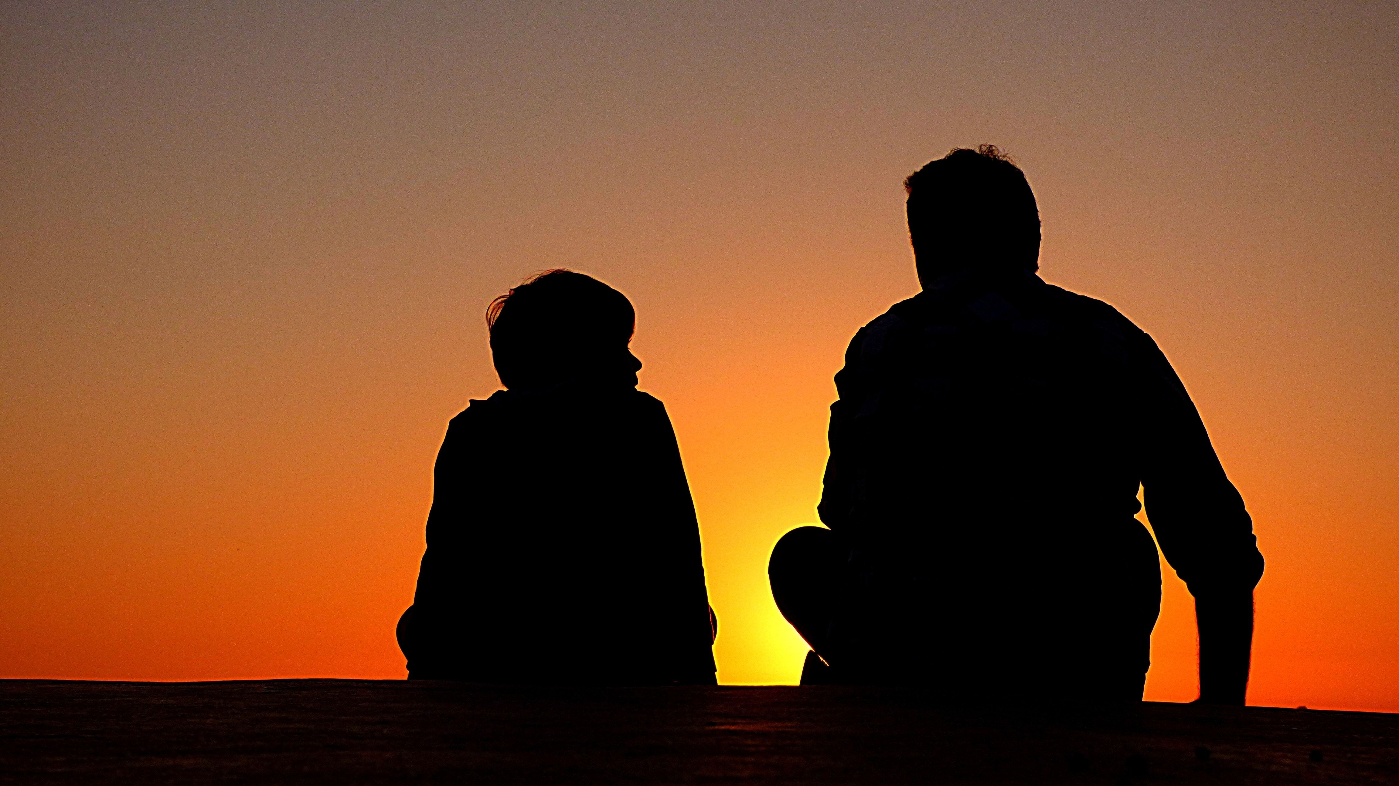 silhouette of boy and man sitting facing sunset free image