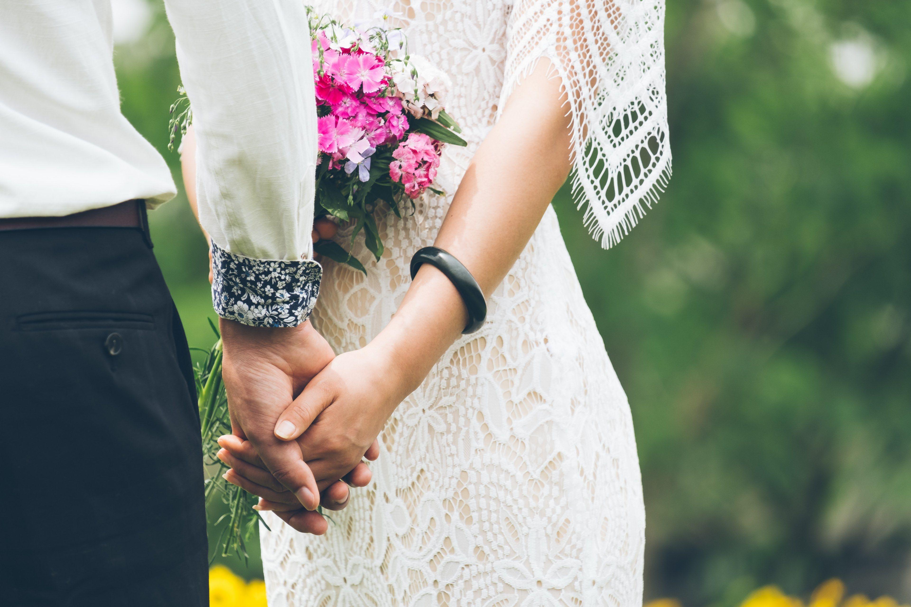 bride with pink bouquet and lace dress hold hands with groombride