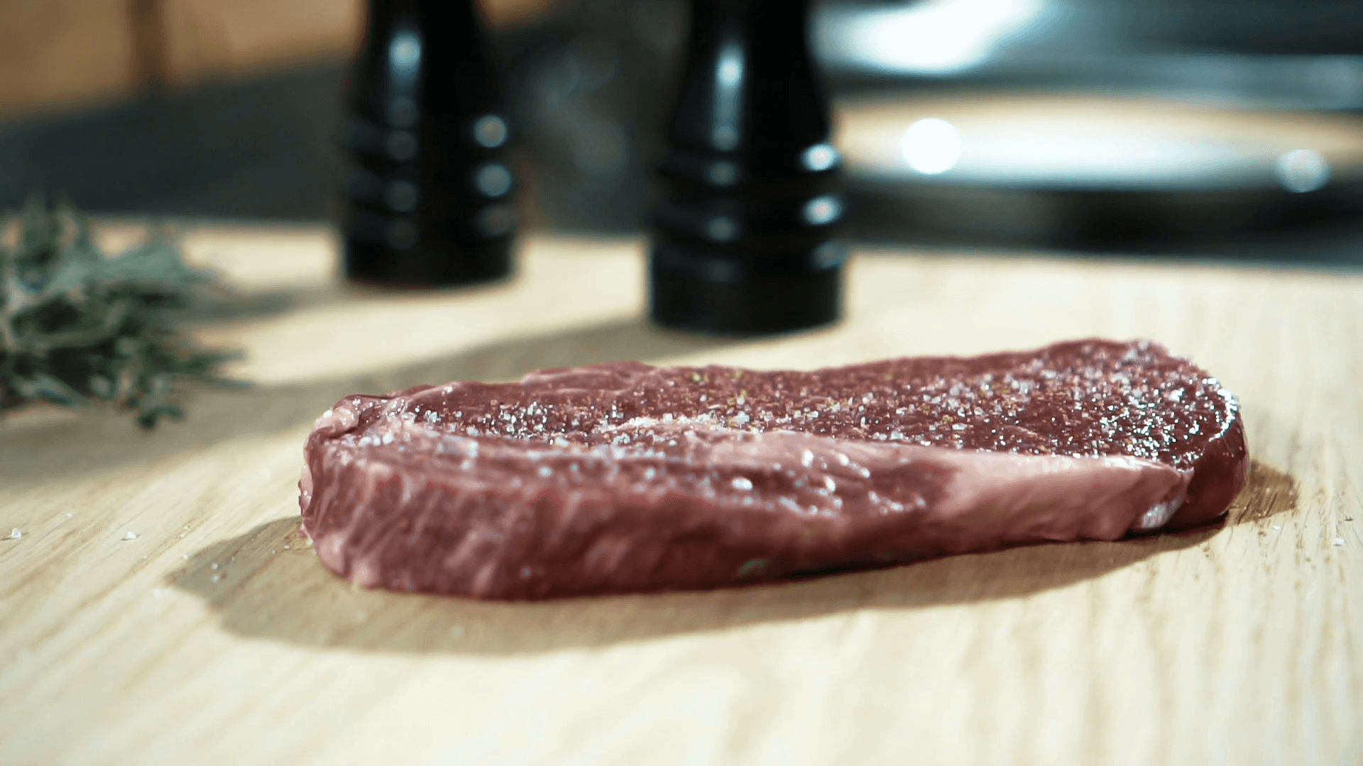 Experienced chef sprinkles piece of meat with greens in kitchen