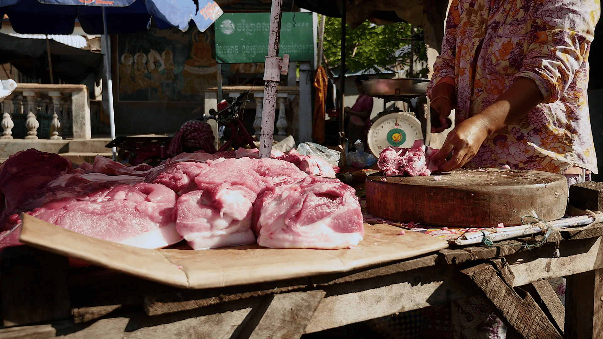 Meat vendor chopping a piece of meat with a hatchet on round wooden