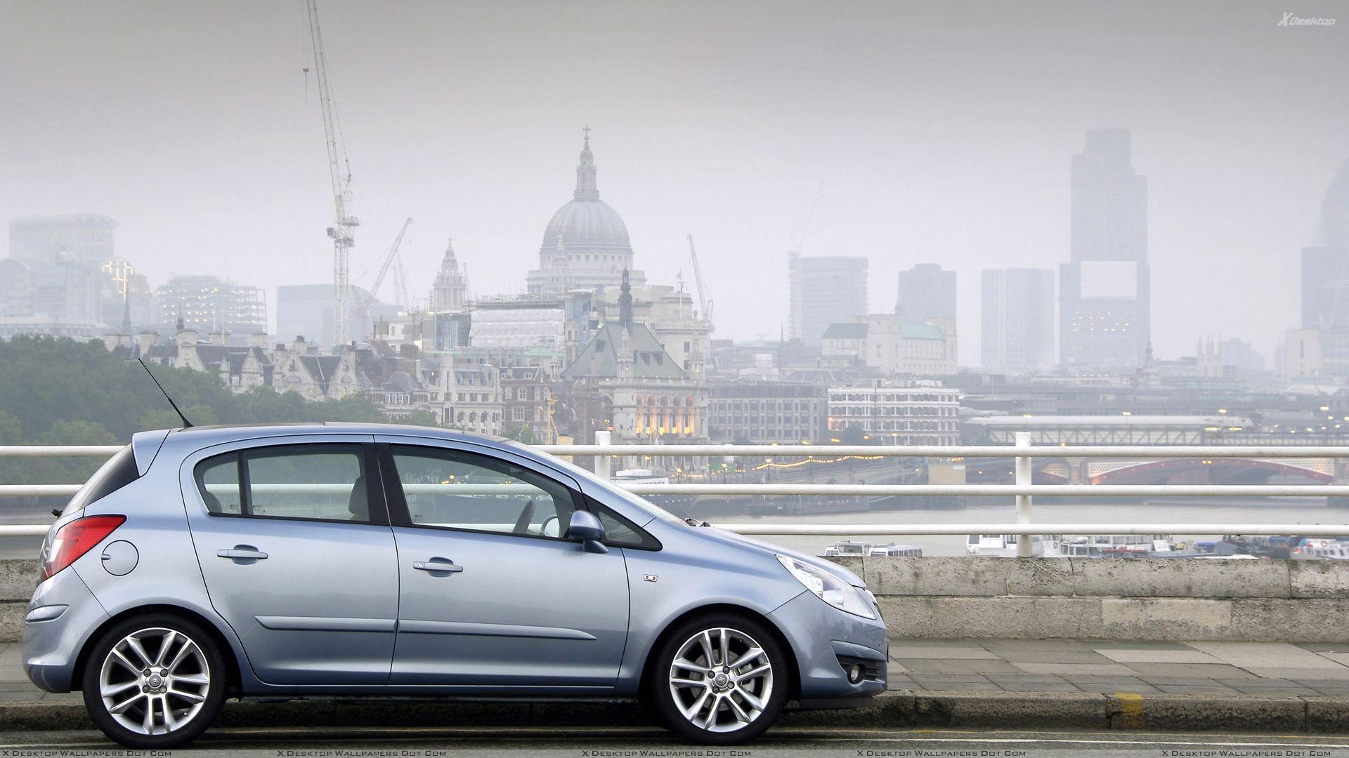 Vauxhall Corsa Side Pose In Blue Near Buildings Wallpaper