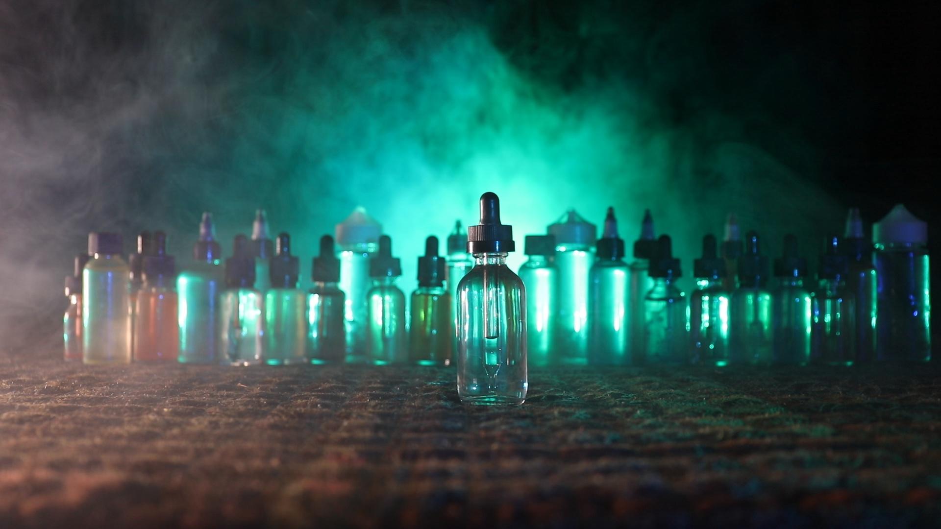 Vape concept. Smoke clouds and vape liquid bottles at dark