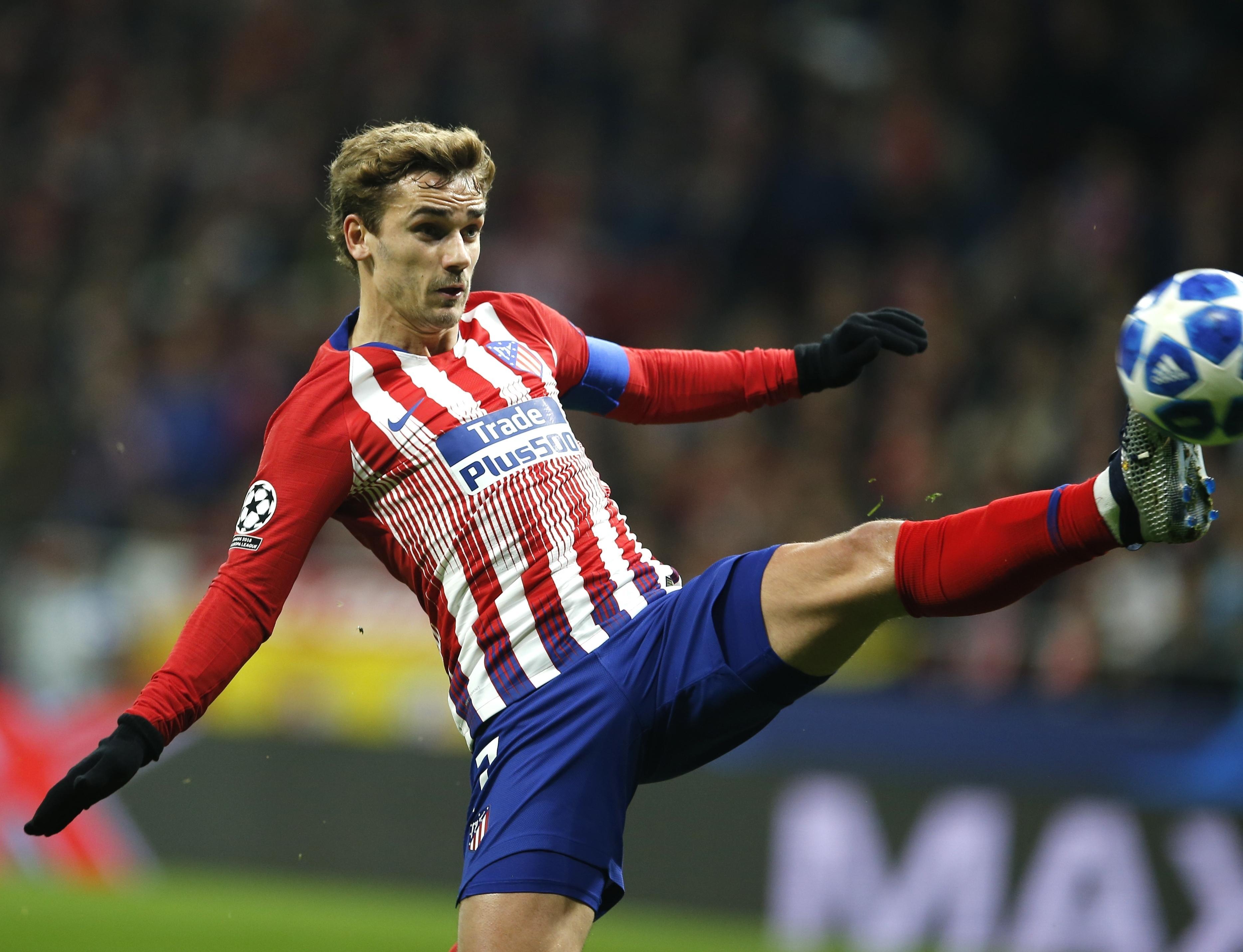  Antoine Griezmann, a soccer player wearing an Atletico Madrid uniform, is in mid-stride kicking a soccer ball.
