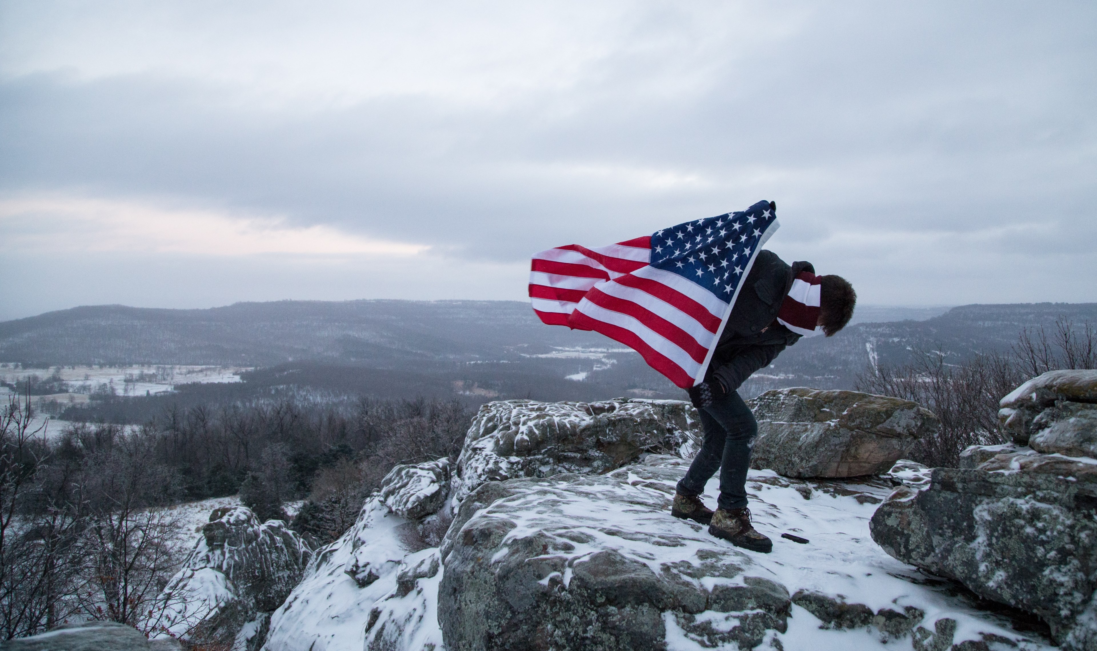 a climber holds the american flag while standing on the peak of a