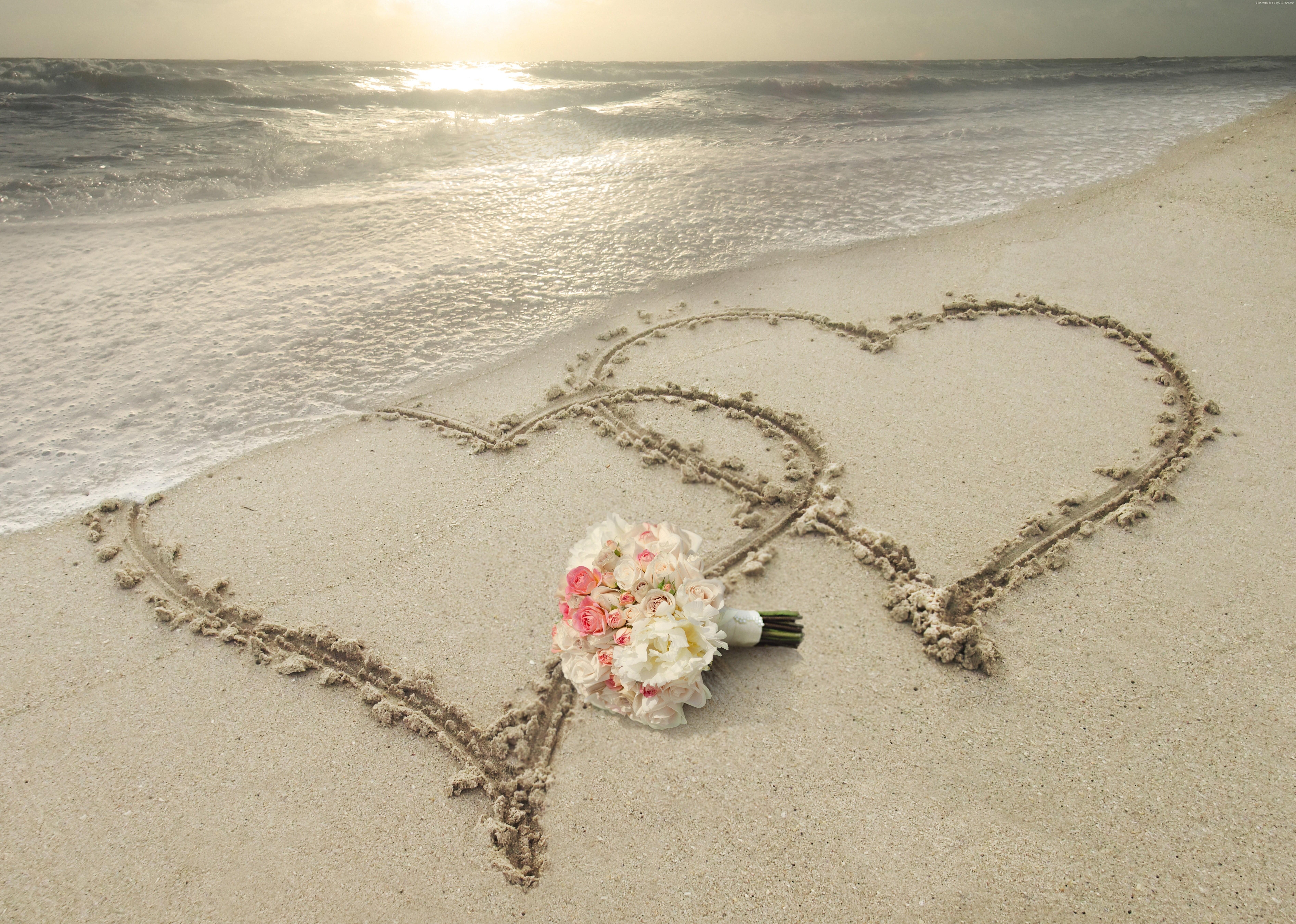 White and pink chrysanthemums bouquet on white sand with two hearts