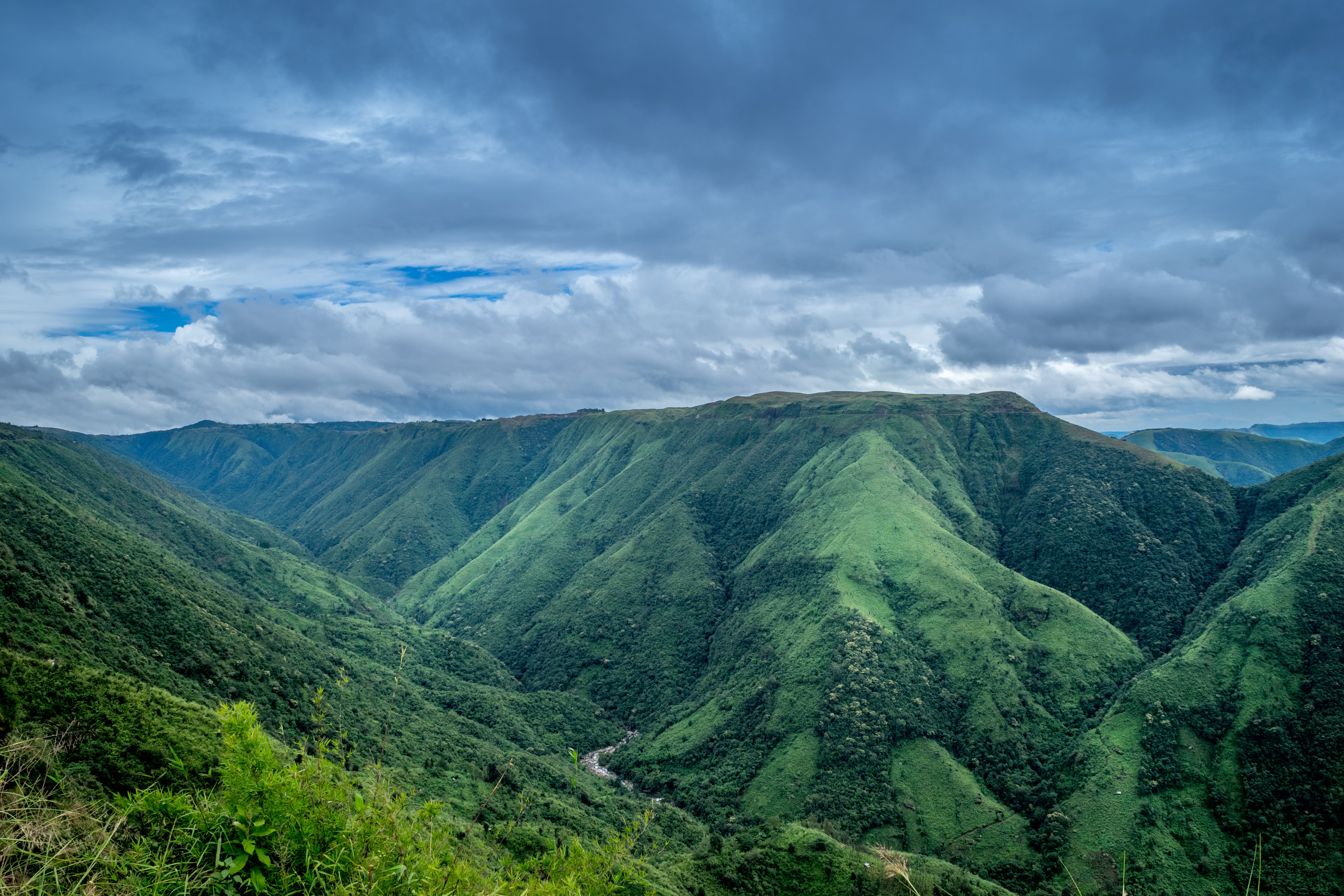 Landscape Photography Of Green Mountains Under Cloudy Sky