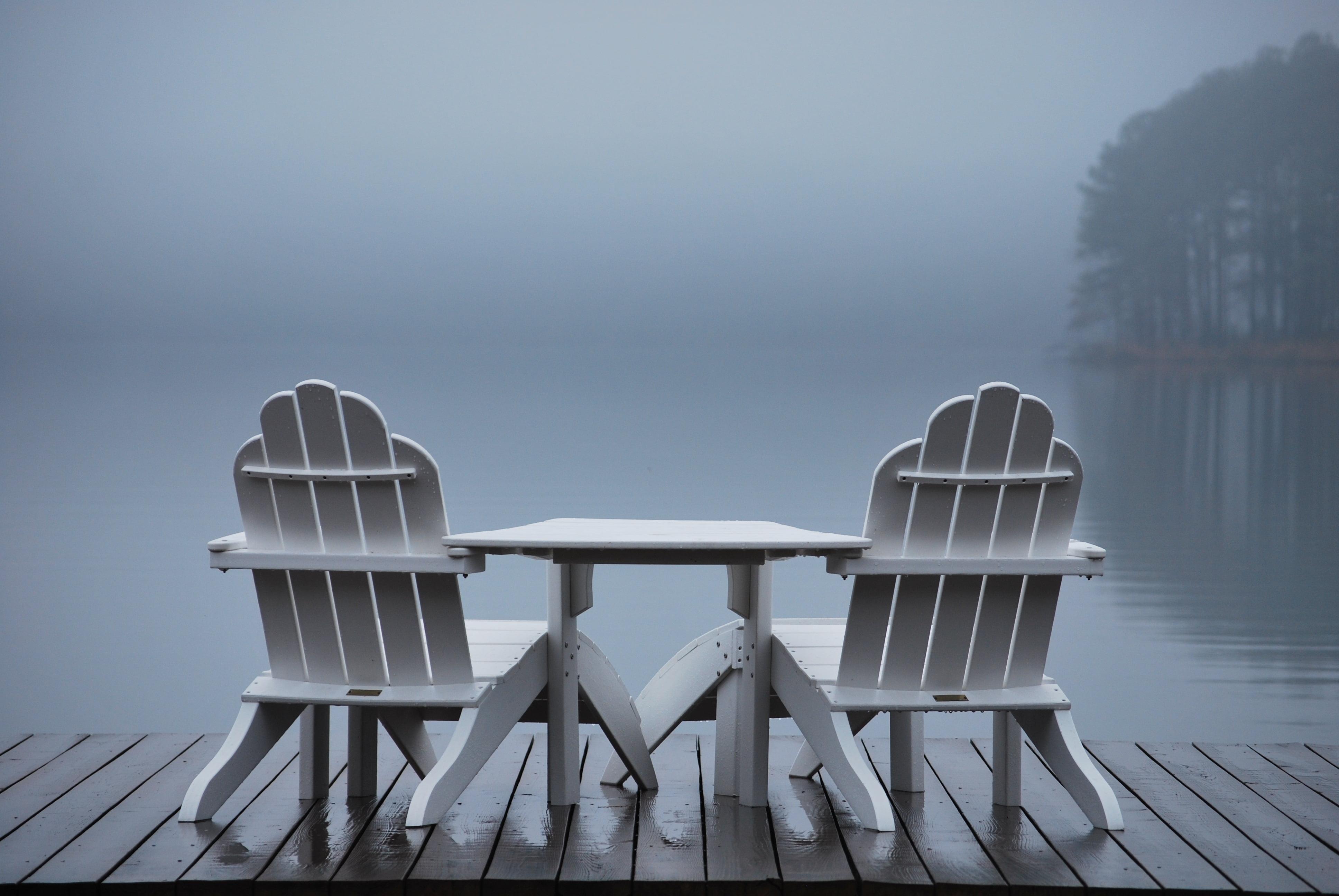 Table in between two adirondack chair on dock facing calm waters