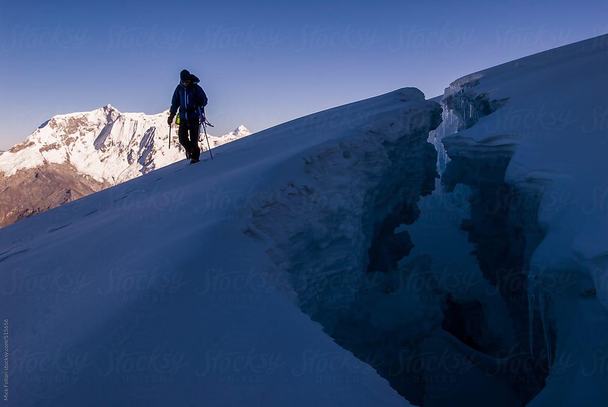 Mountain climber near large crevasse with peaks behind.