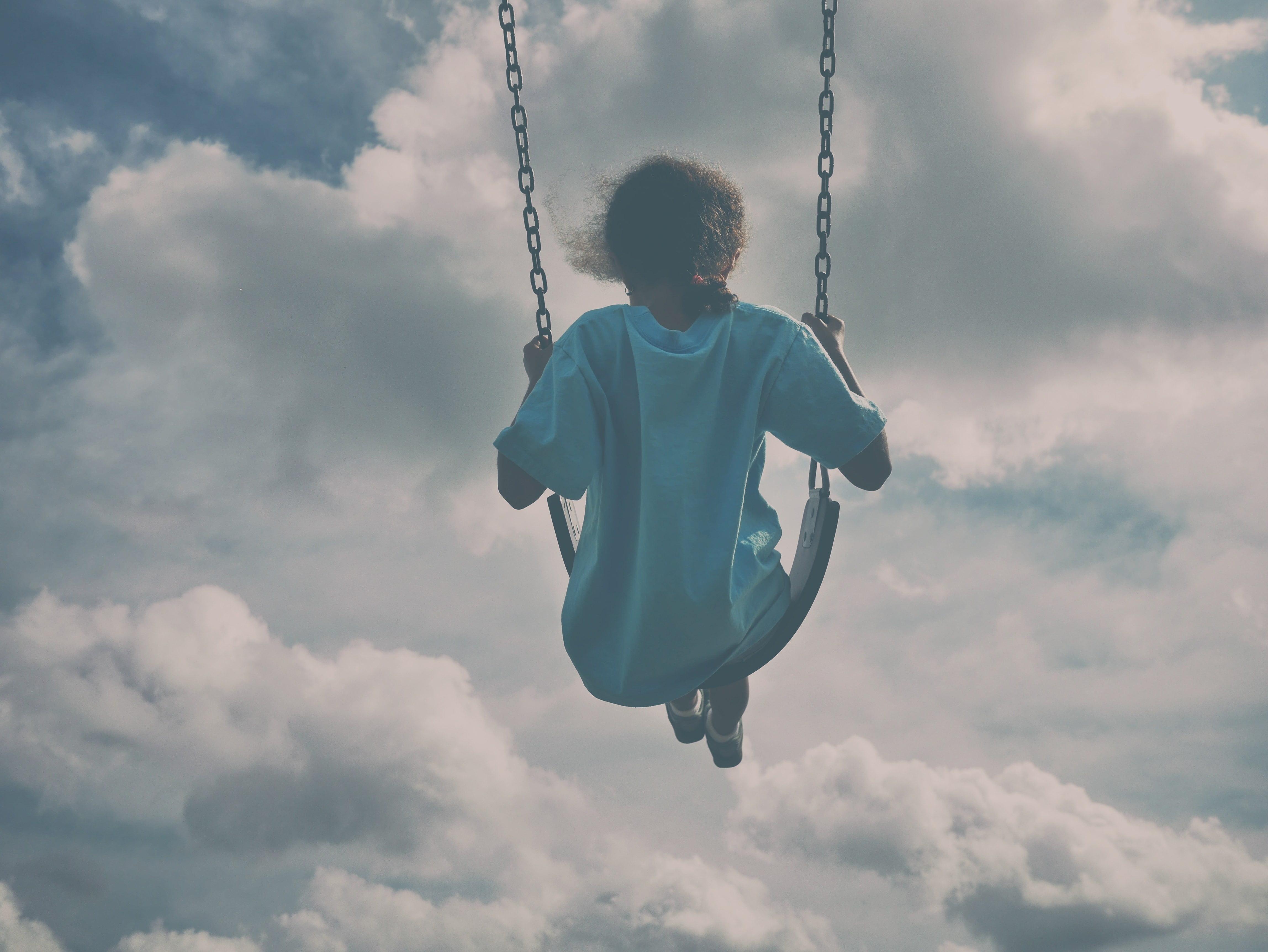 Girl in white shirt sitting on swing under gray clouds HD wallpaper